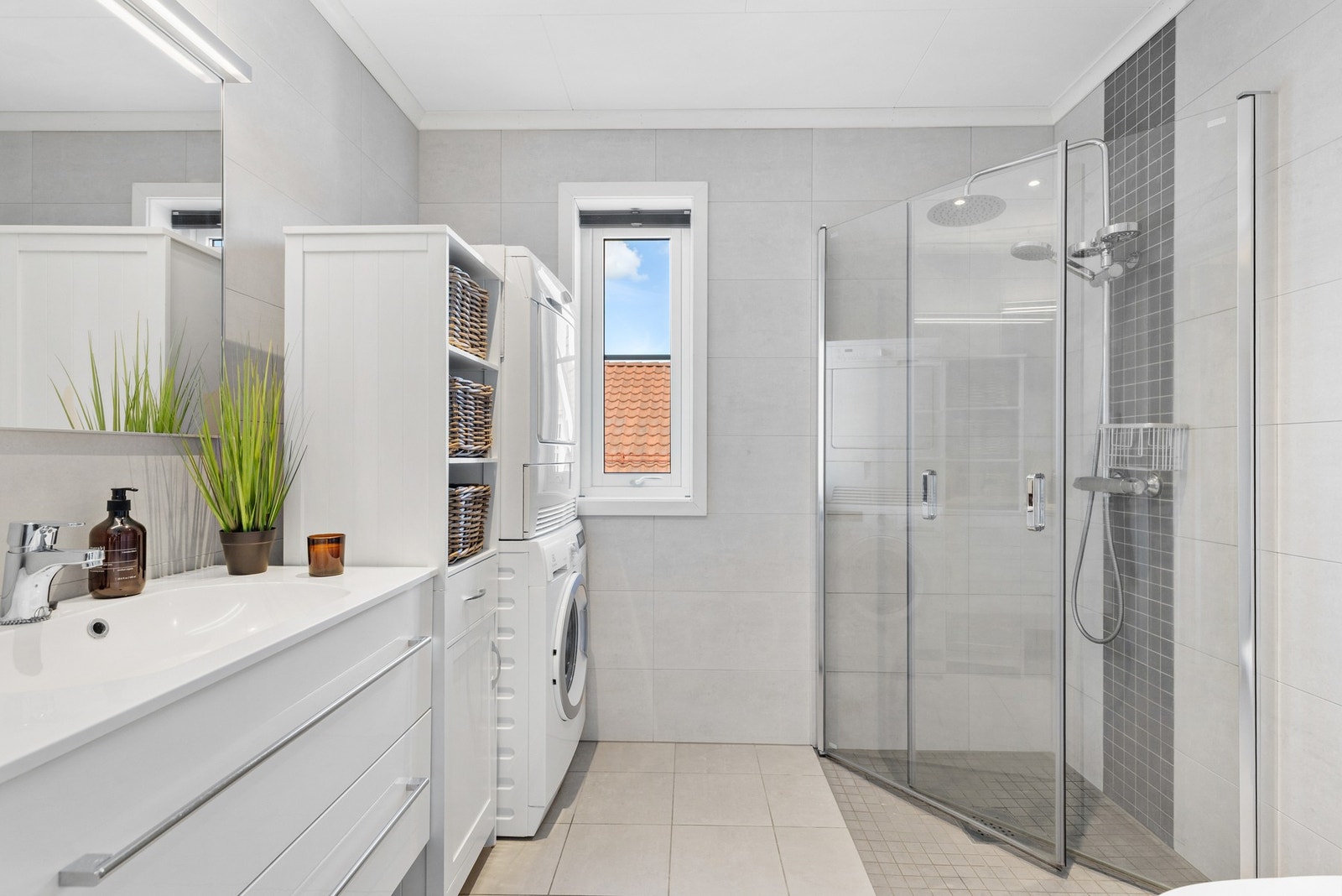 Delikat, helfliset bad innredet med dushjørne med glassdører og opplegg for vaskemaskin og kondenstørketrommel Galleribilde