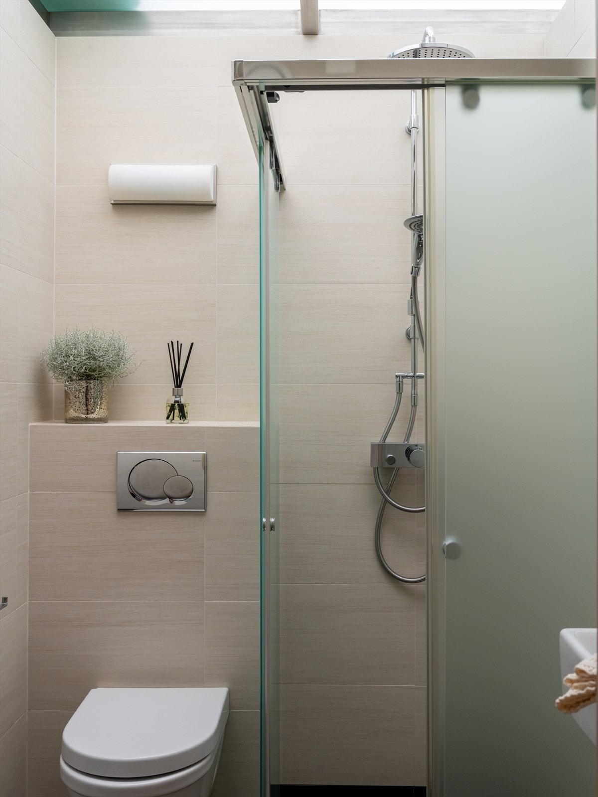 Badet nærmest gangen er innredet med vegghengt toalett og dusjnisje i frostet glass, to-greps dusjarmatur på vegg og regnfallsdusj Galleribilde