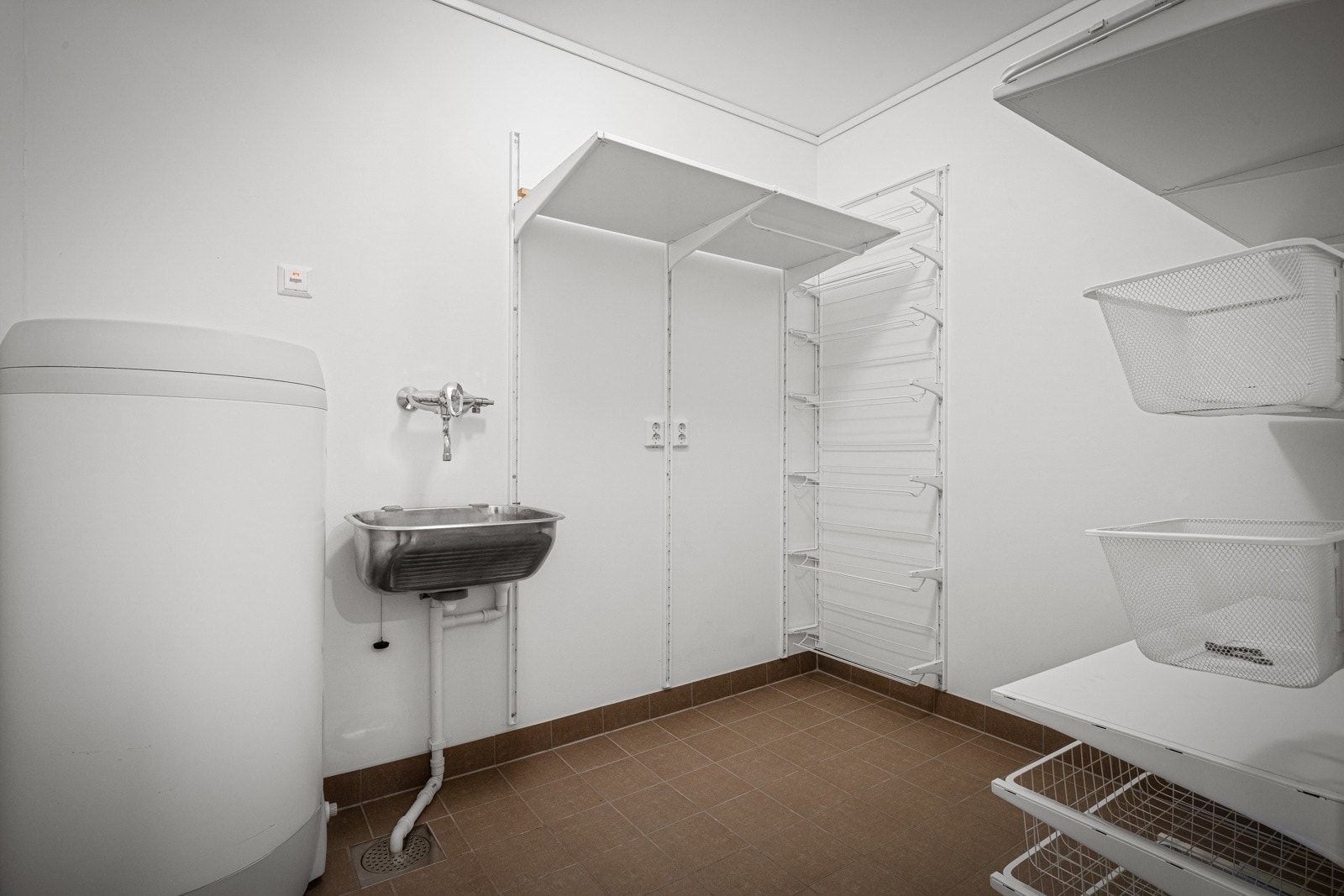 Vaskerom med fliser og varmekabler, opplegg for vaskemaskin, samt hylleinredninger for praktisk oppbevaring. Galleribilde