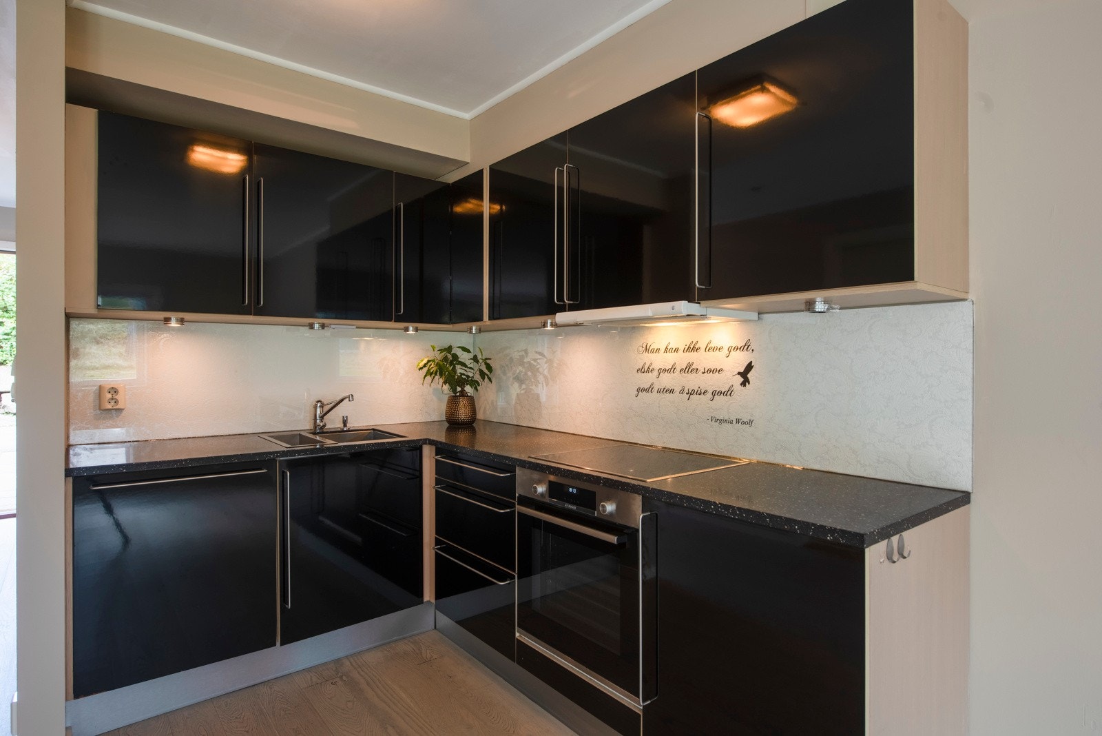 Kjøkkenet er oppført i en funksjonell L-form med god arbeidsflyt og skapplass. Innredningen har sorte, glatte fronter og grå benkeplate av laminat med dobbel oppvaskkum. Galleribilde