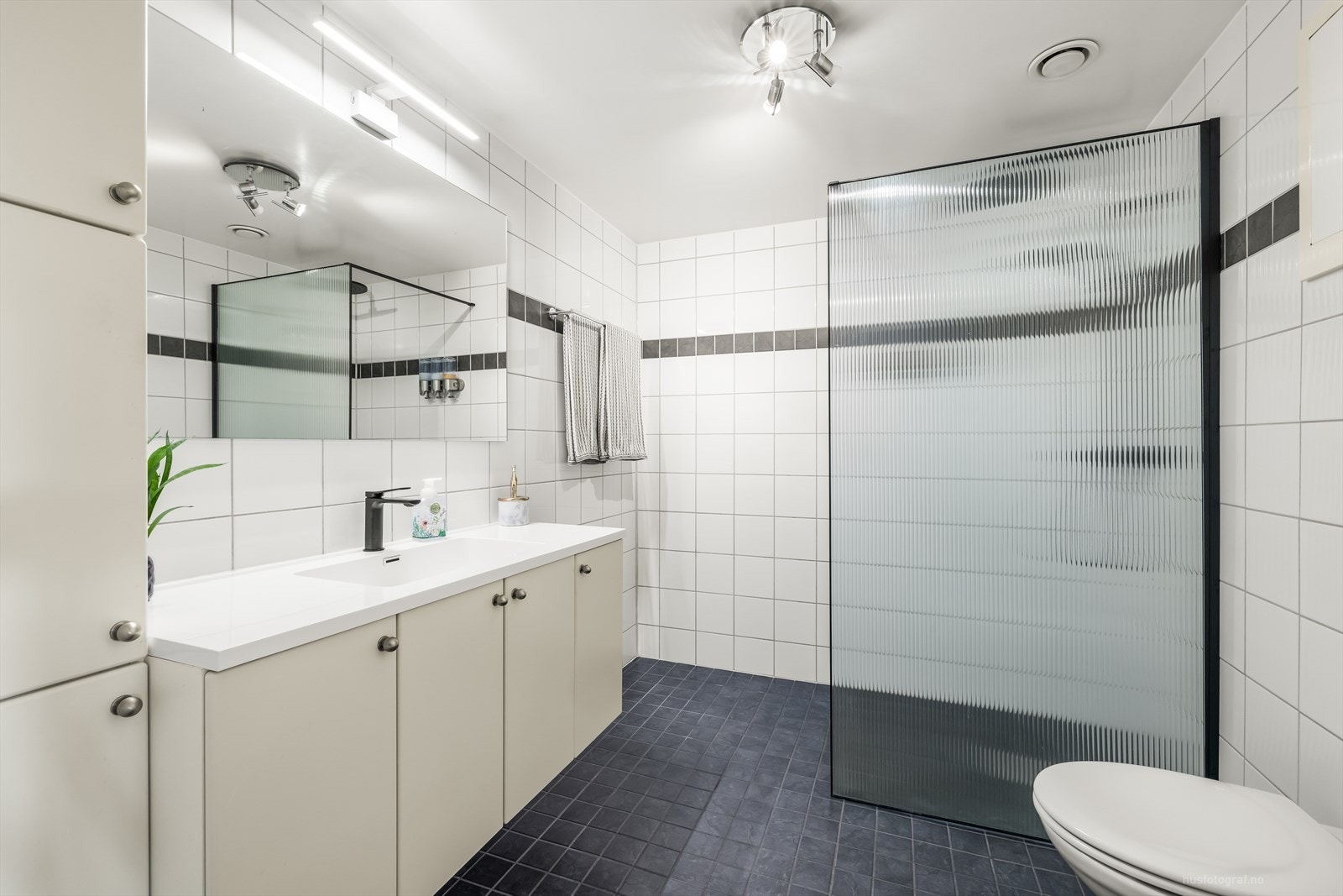 Badet er utstyrt med dusjhjørne med dusjvegg og vegghengt toalett. Galleribilde