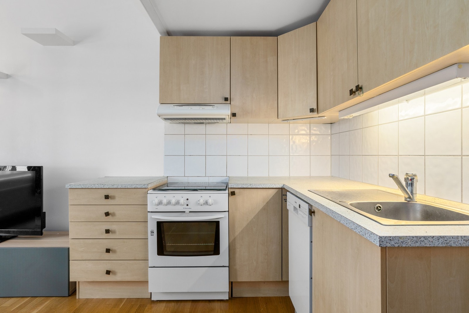 Kjøkkeninnredningen er enkel, med beige, glatte fronter, laminert benkeplate og nedfelt oppvaskkum. Galleribilde