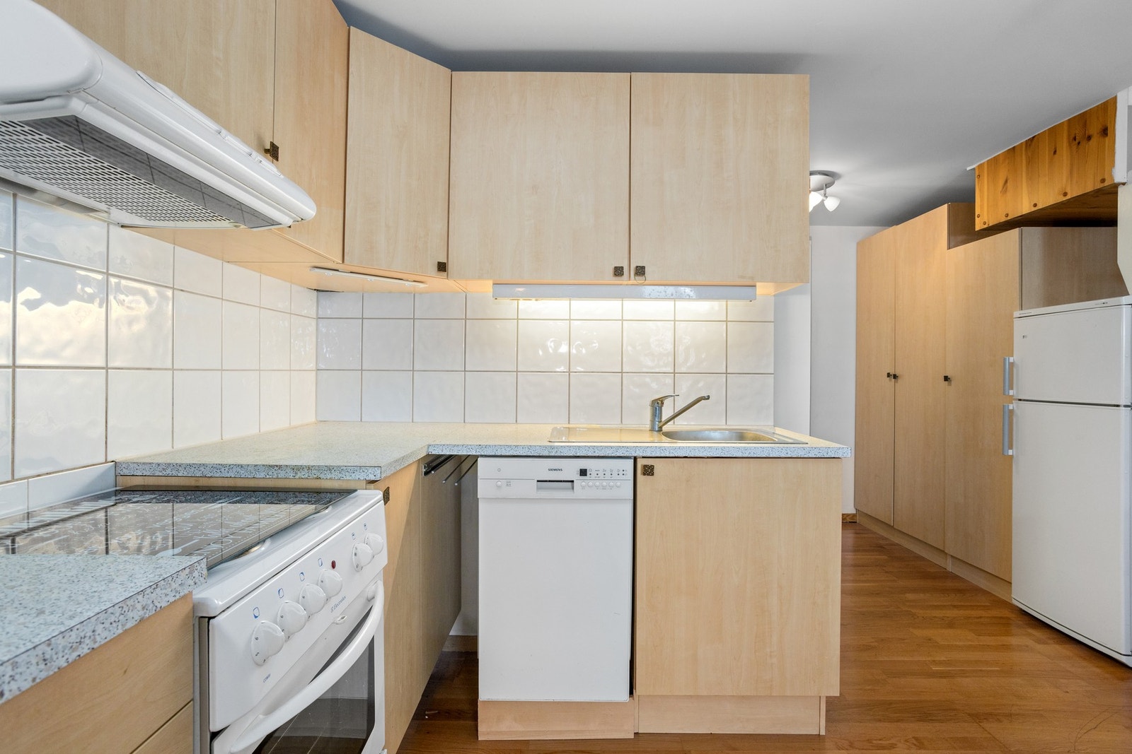 Det er montert belysning og hvite fliser over benken, og over komfyren har kjøkkenet en ventilator med kullfilter. Galleribilde