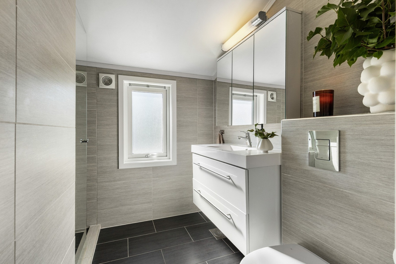 Moderne baderom med lyse fliser, stort speilskap og servant med skuffer. Galleribilde