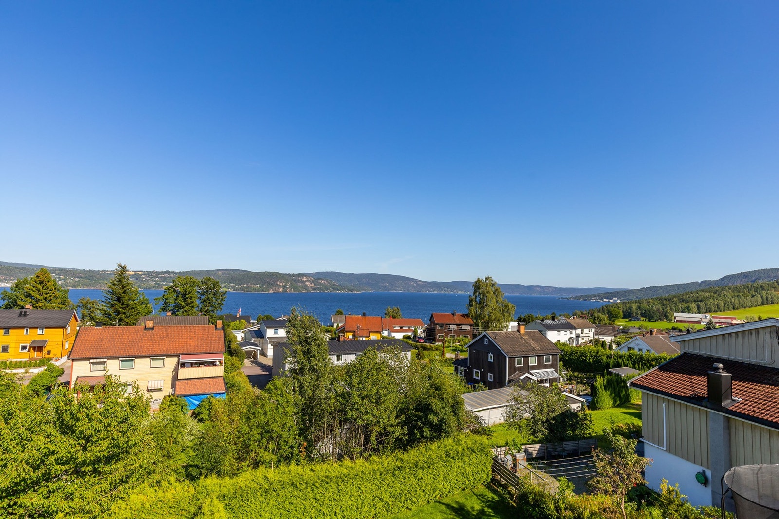 Utsikt over nabolag med sjø i bakgrunnen, omgitt av skog og åser Galleribilde