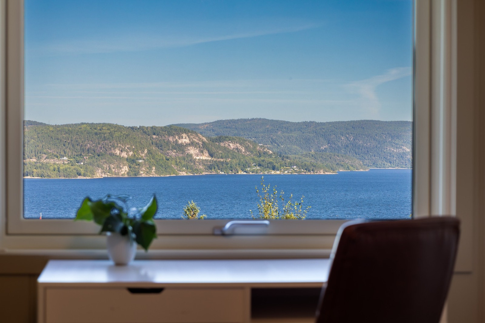 Utsikt over fjord og skogkledde åser gjennom vindu. Galleribilde