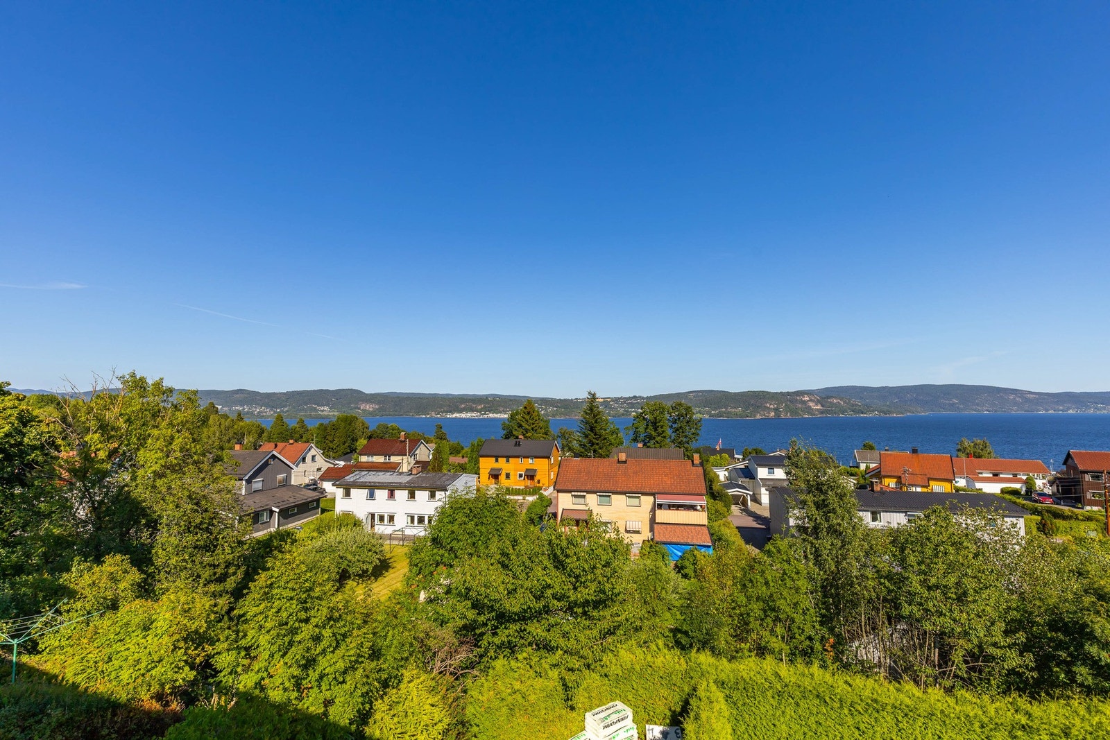Utsikt over boligområde med sjø og åser i bakgrunnen. Galleribilde