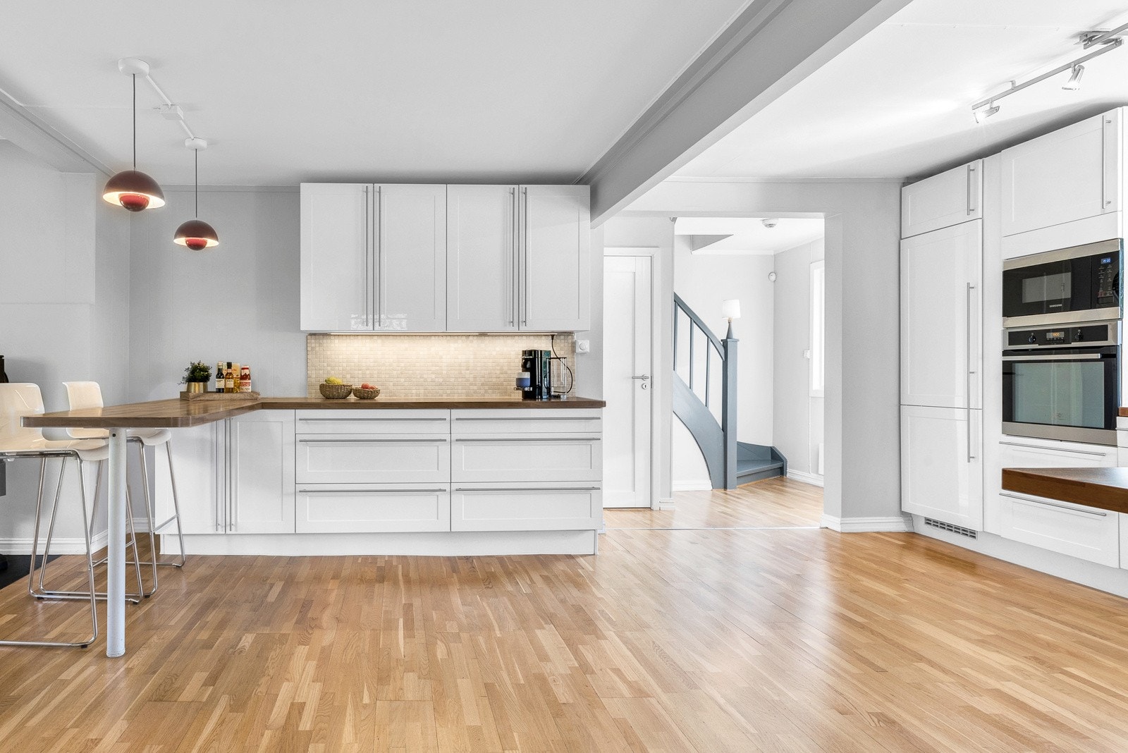 Kjøkkeninnredningen er montert langs tre vegger og har i tillegg halvøy med barløsning og sitteplasser. Skap og skuffer har hvite, profilerte høyglansfronter. Galleribilde