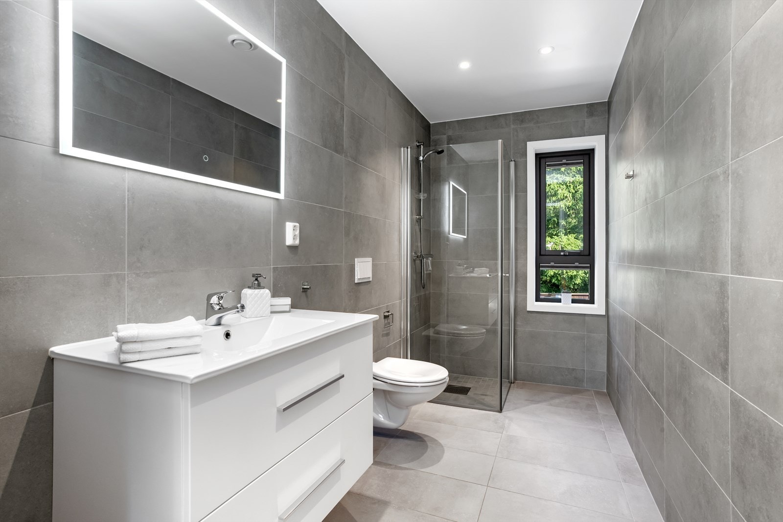 Dobbelt underskap med praktiske kolonialskuffer, stilrene kvadratservantbenker og veggspeil med omramming av LED-lys gir god oppbevaringsplass. Innfelte downlights i himlinger i begge rom gir suverent lys i tillegg til lyset i speilene. Galleribilde