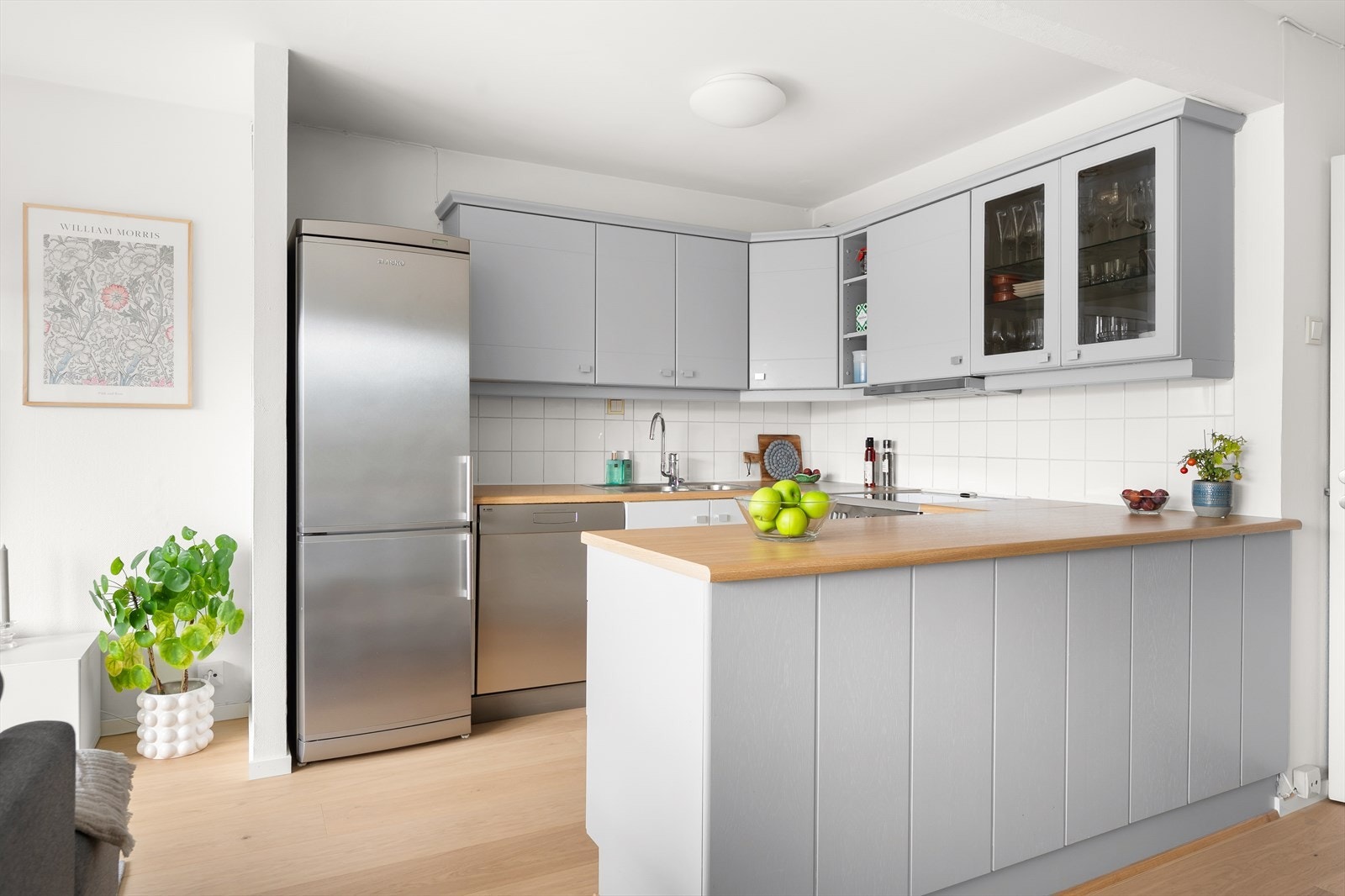 Kjøkkeninnredning med glatte, malte fronter, fliser på vegg over kjøkkenbenken og benkeplate i laminat. Galleribilde