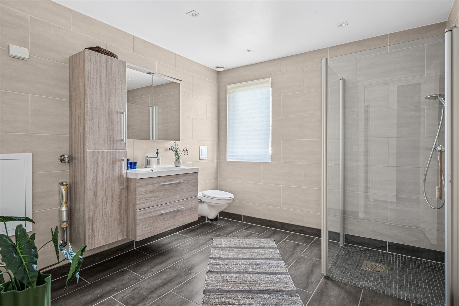 Badet er innredet med veggmontert toalett, dusjhjørne med vegger/dører i herdet glass, med nytt høyskap, servantinnredning og overskap med speilfronter og belysning. Galleribilde
