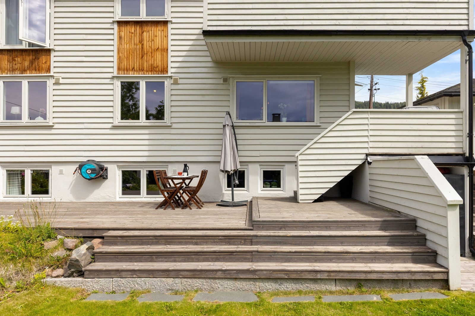 flott vestendt uteplass med plass til utemøblement og grill med trapp ned til en gresslagt hage Galleribilde