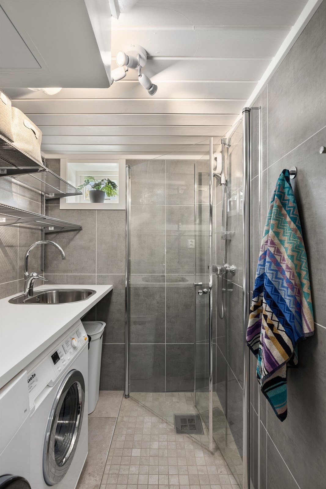 Flislagt vaskerom med blant annet opplegg til vaskemaskin, plass til tørketrommel og et dusjhjørne Galleribilde