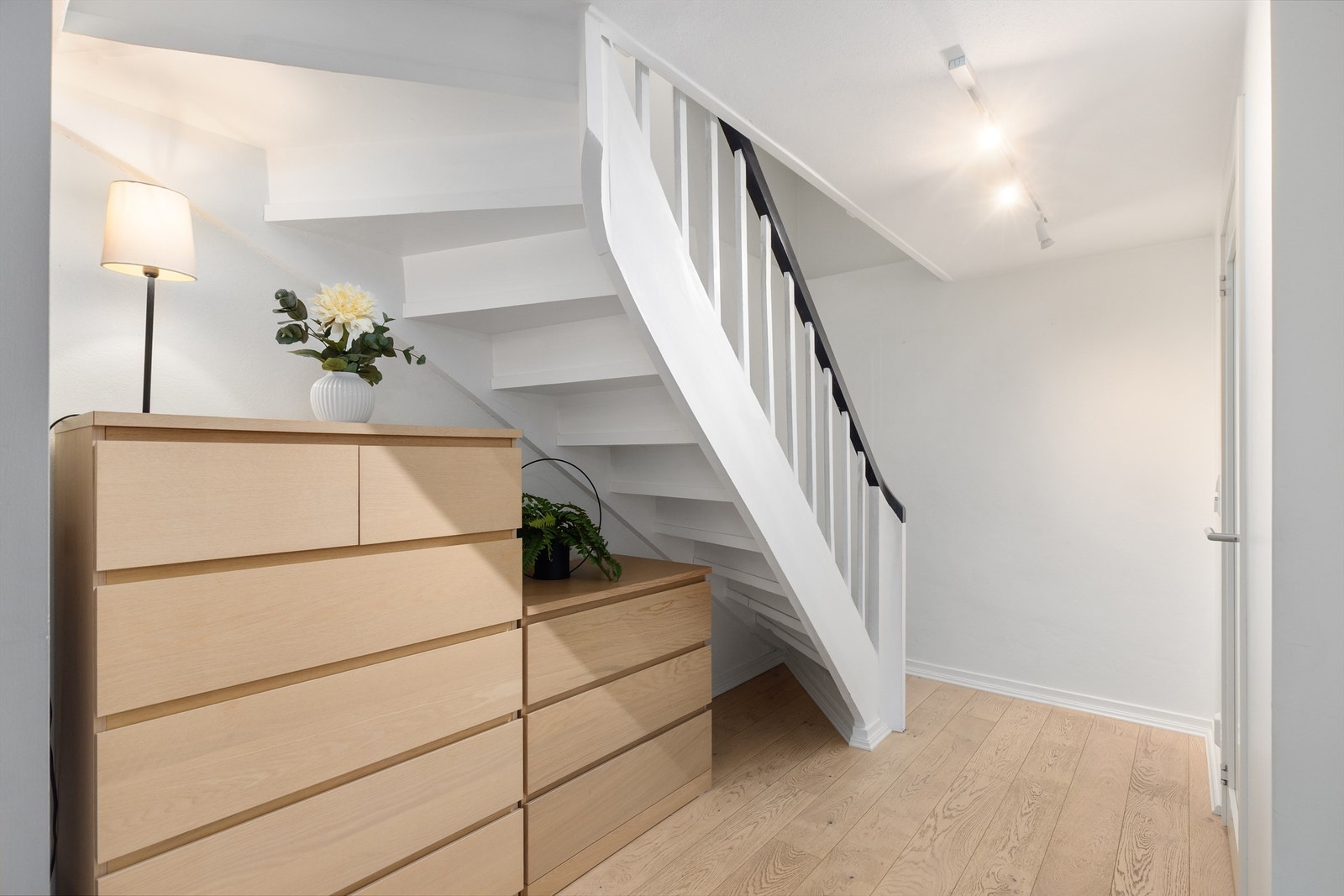 Trappegang med en klassisk hvitmalt trapp med stort håndløper. Plass til kommoder for lagring under trapp. Galleribilde