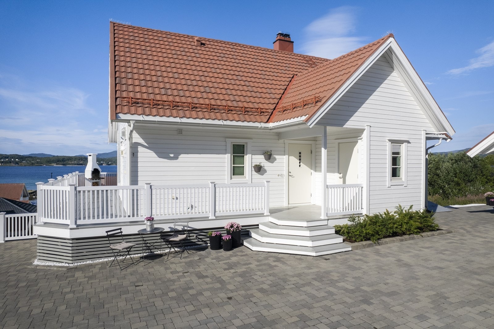 Pent eksteriør med steinlagt gårdsplass og plen med beplantninger. Galleribilde