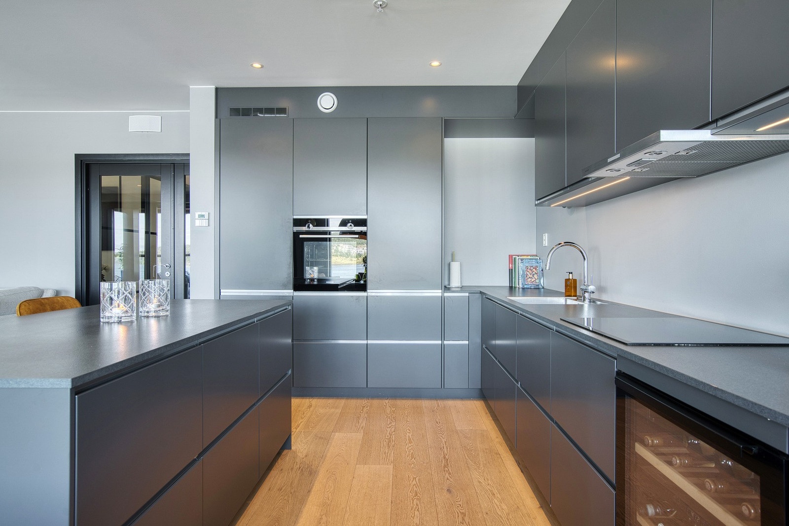 Den åpne kjøkkenløsningen avgrenses med en kjøkkenøy, som både gir ekstra arbeidsflate og fremhever kjøkkenets estetikk. Galleribilde