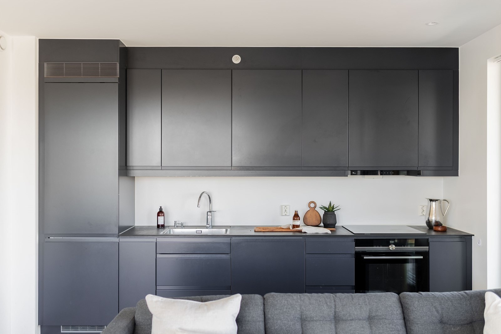 Kjøkkenet har en stilren innredning fra kvalitetsleverandøren Sigdal med mørke slette fronter og laminert benkeplate med underlimt vask. Galleribilde