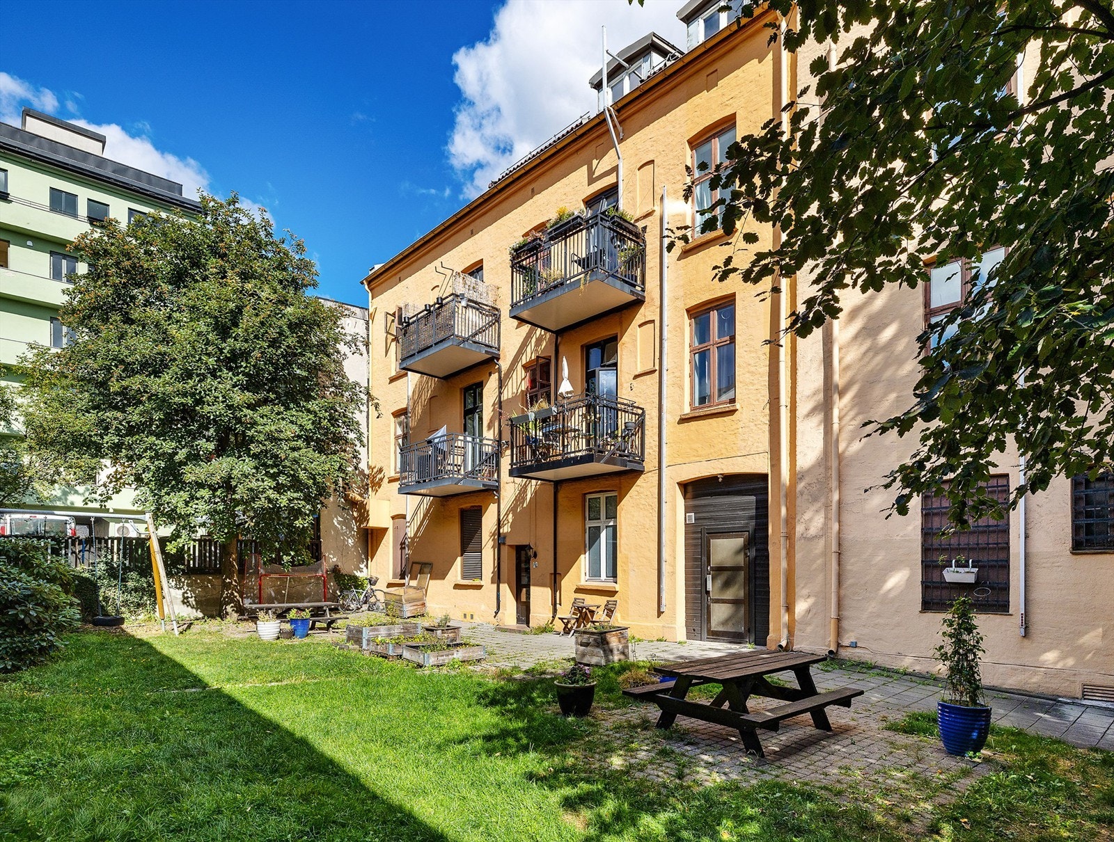 Hyggelig og frodig opparbeidet bakgård med blomsterkasser, benk og lekeapparat og sandkasse. Galleribilde