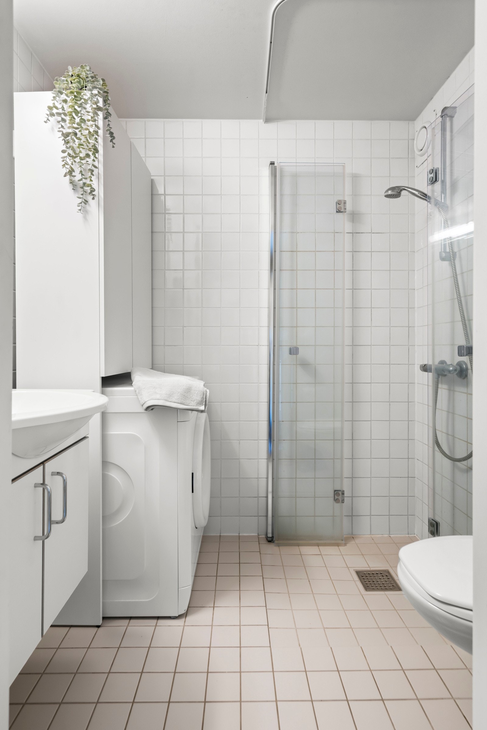 Baderommet fremstår som moderne med lyse fliser og opplegg for vaskemaskin. Galleribilde