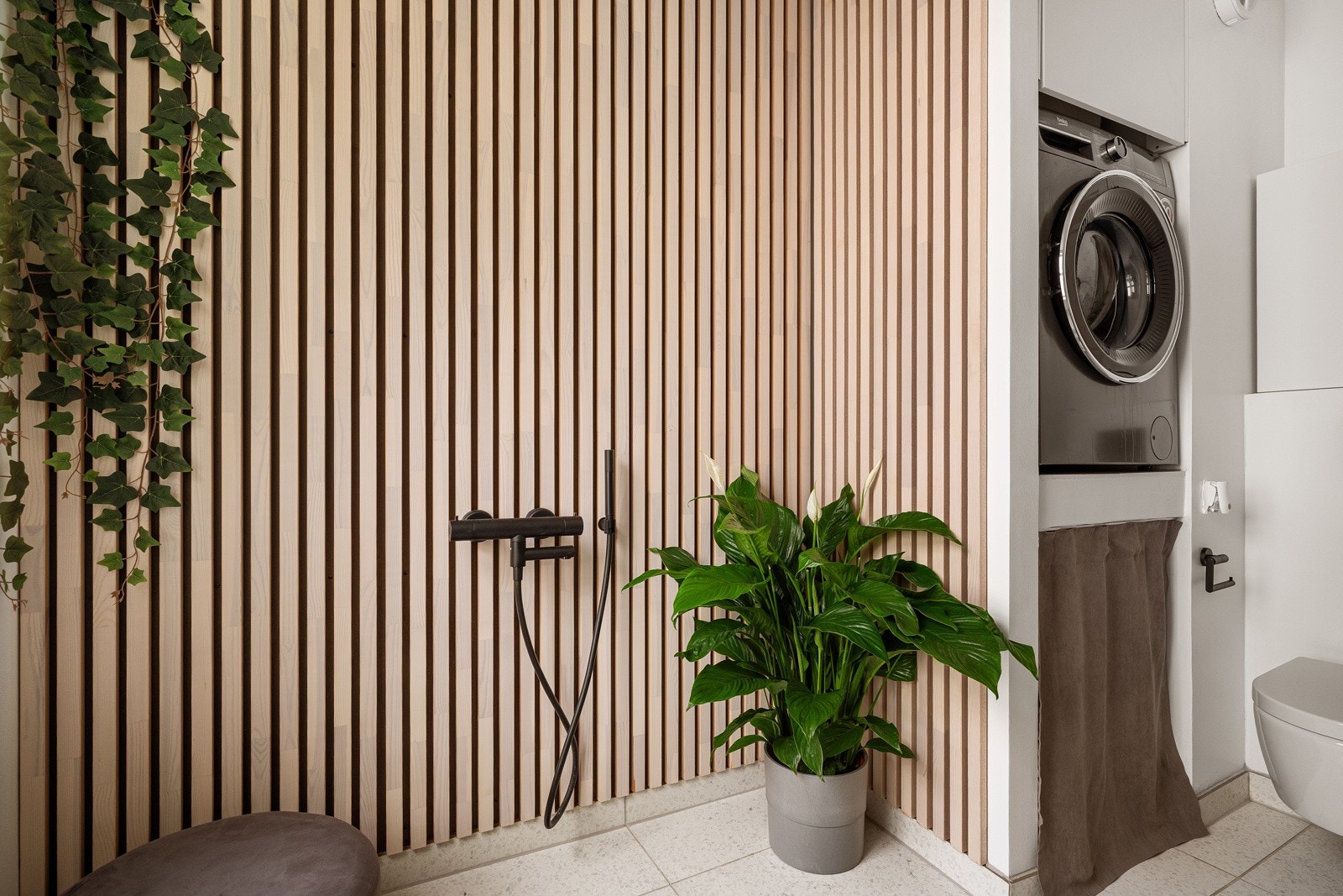 Dusjhjørne med regnfalldusj, vegghengt toalett, opplegg for badekar og opplegg for vaskemaskin. Galleribilde