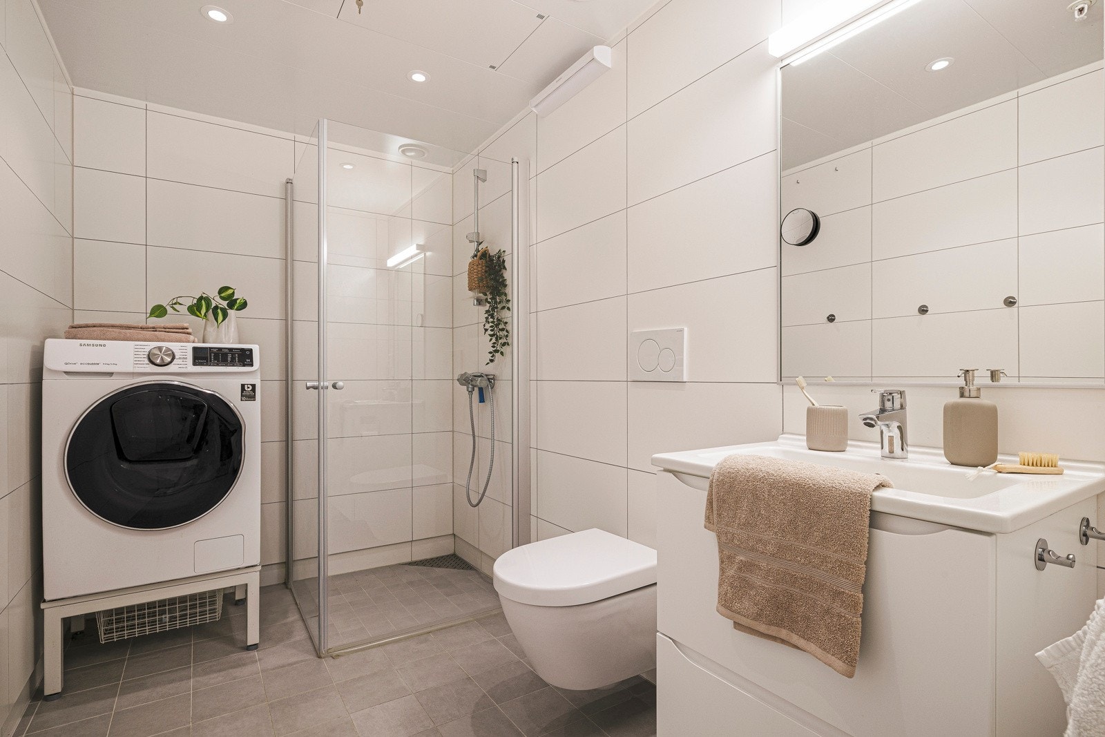 Helfliset bad på 4,9 kvm med gulvvarme. Badet har stålplater i himling med innfelte downlights og er innredet med vegghengt toalett, baderomsinnredning med nedfelt servant, dusjhjørne og opplegg for vaskemaskin. Galleribilde