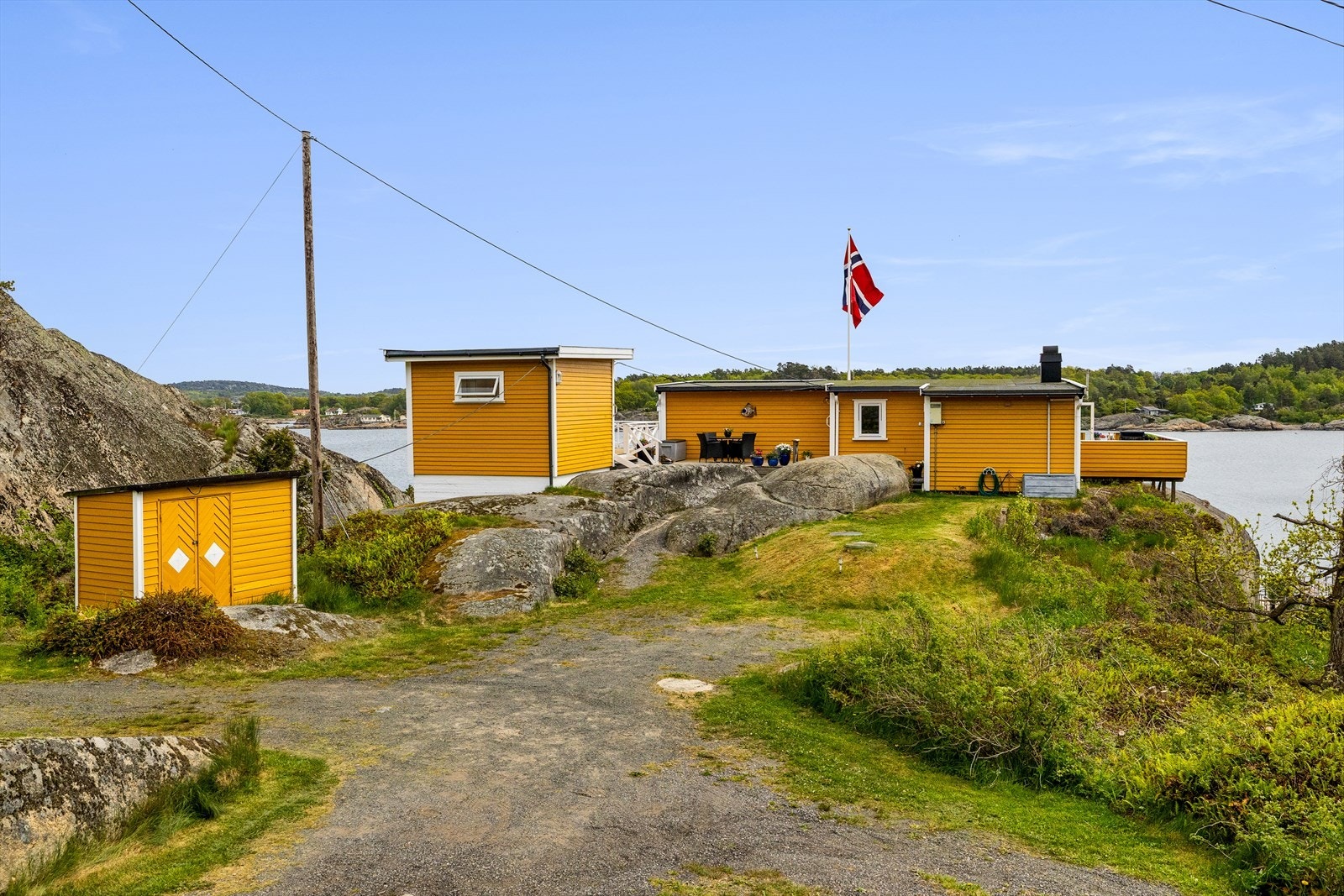 Tomten ligger høyt og fritt, bebygd med hytte, anneks og utebod, alle malt i en glad gulfarge med hvit staffasje. Galleribilde