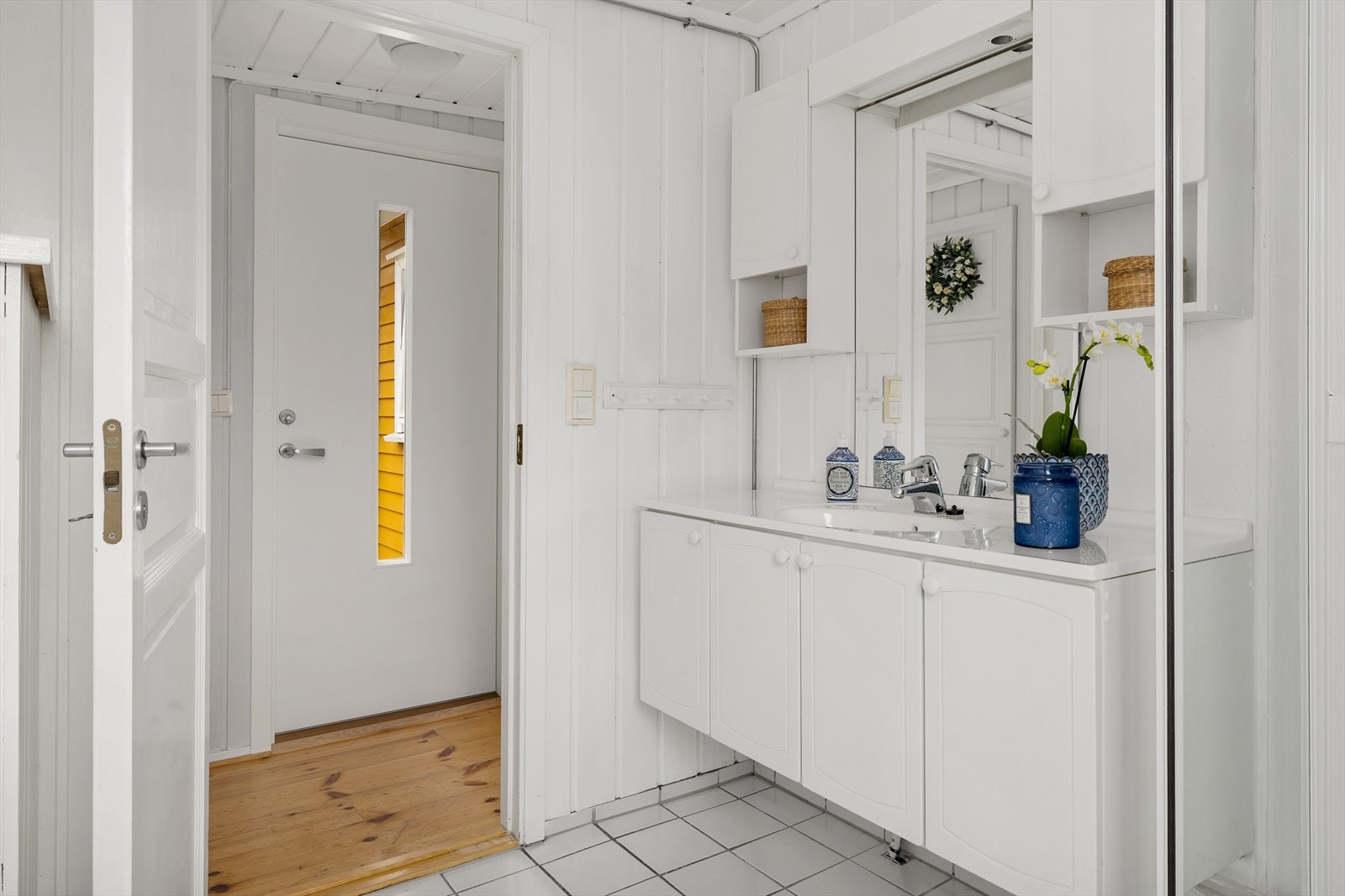 Badet har lyse fliser på gulvet, hvitmalte paneloverflater og hvit innredning med god skapplass. Galleribilde