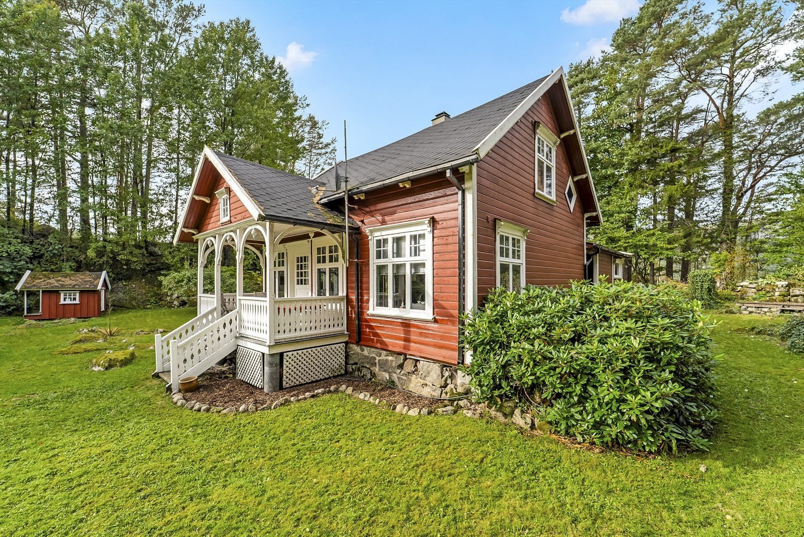 Sjarmerende rød trehytte med overbygd veranda, omkranset av frodig natur. Perfekt for deg som søker ro og naturskjønn beliggenhet. Galleribilde