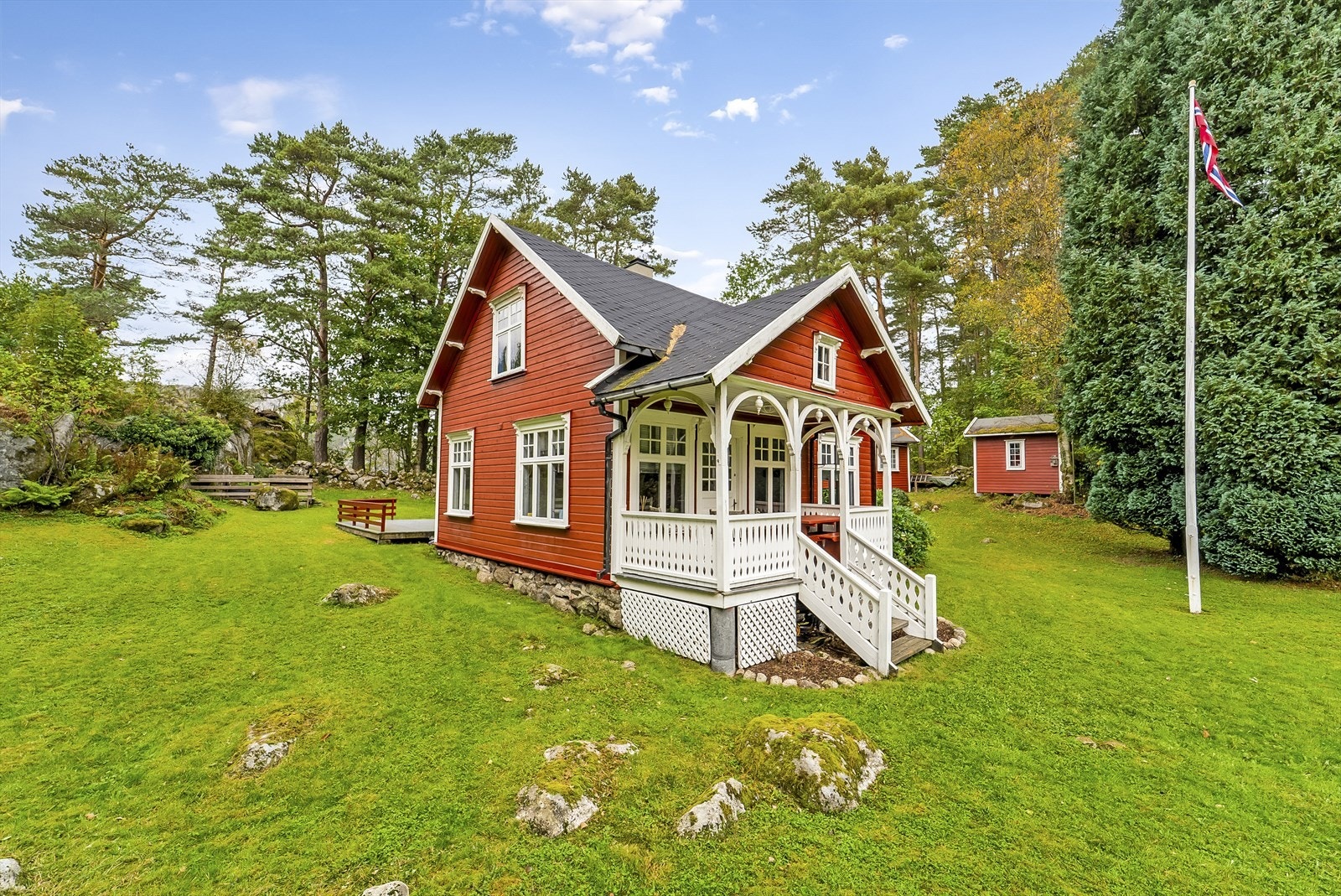 Sjarmerende rød trehytte med hvite detaljer, idyllisk beliggende i frodig natur og sjøen som nærmeste nabo. Galleribilde