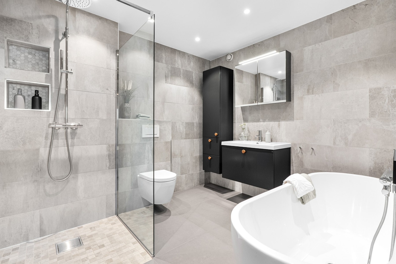 Lyst og moderne bad med dusj, badekar, vegghengt toalett og servant med speilskap. Galleribilde