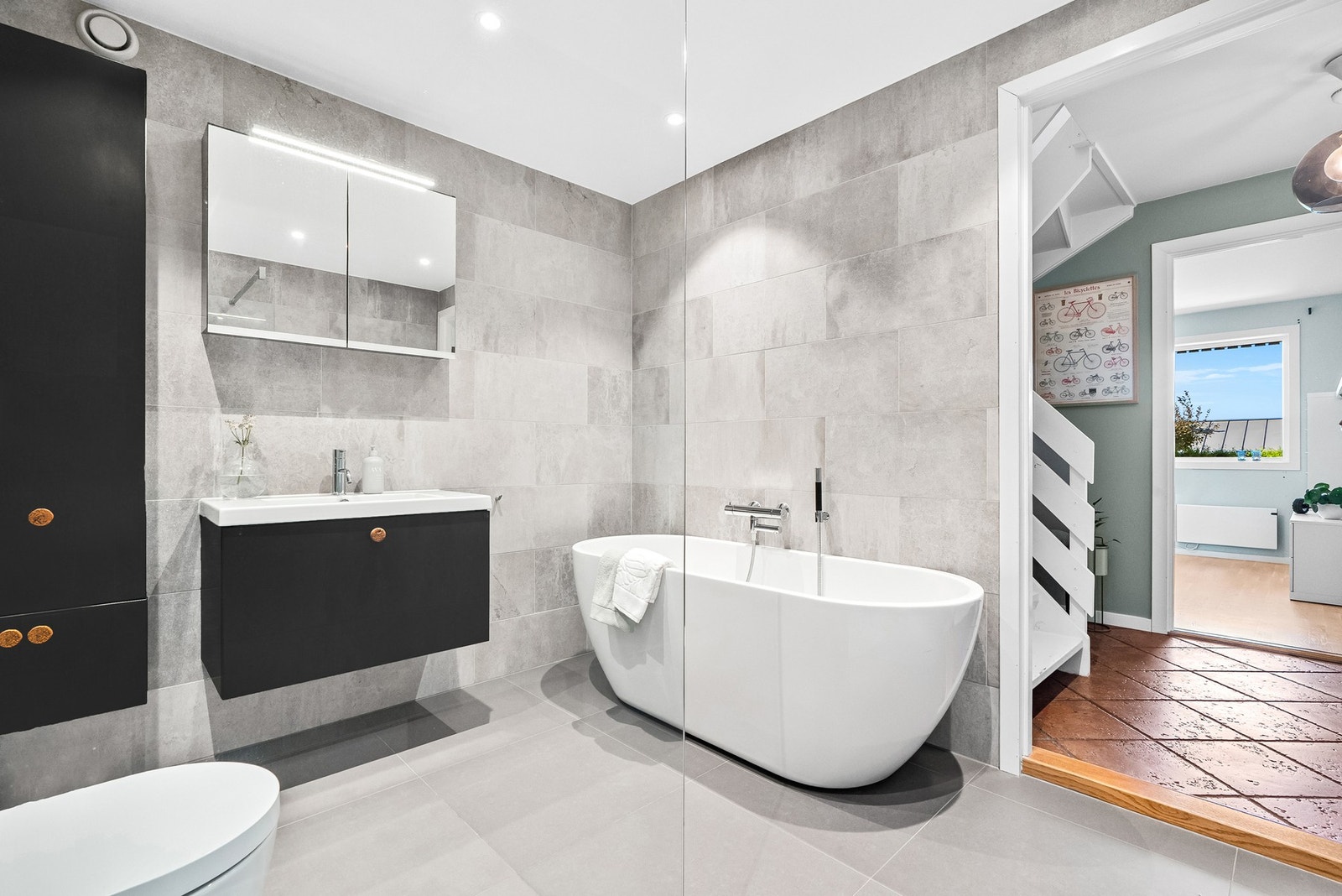 Moderne bad med frittstående badekar, vegghengt servant og speilskap. Flislagte vegger og gulv med spotbelysning. Galleribilde