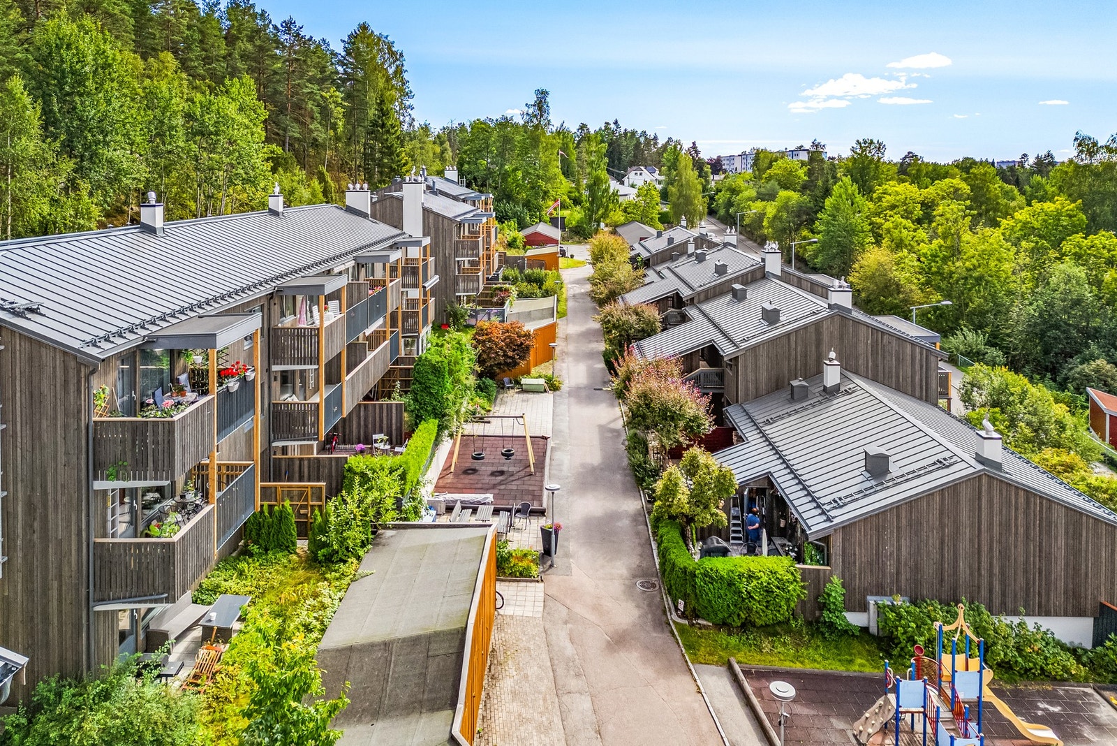 Rekkehus med moderne fasade og balkonger, omgitt av grøntområder og lekeplass. Galleribilde