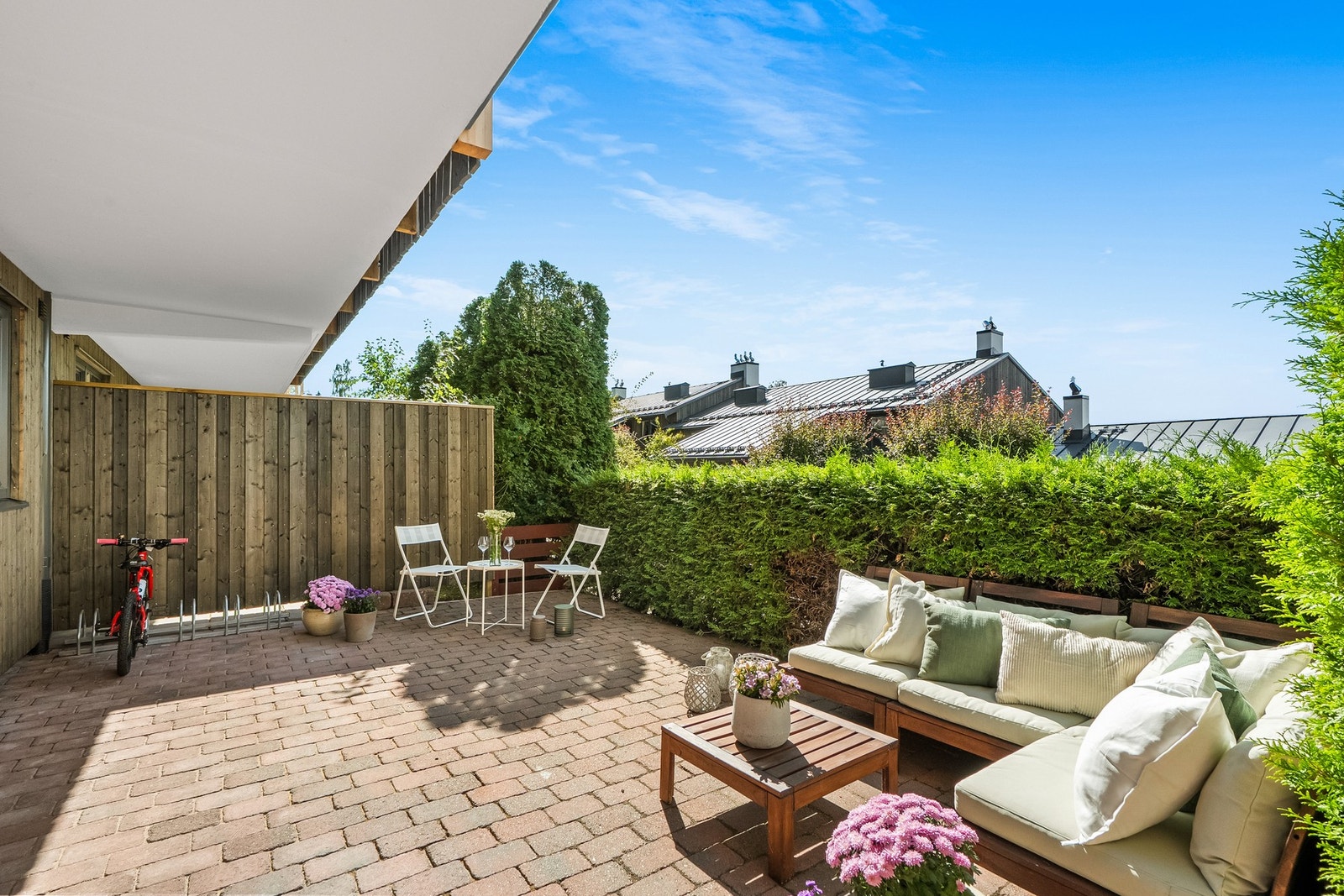 Romslig uteplass med belegningsstein og sittegruppe. Grønn hekk gir skjerming. Lys og luftig atmosfære med utsikt mot natur. Galleribilde