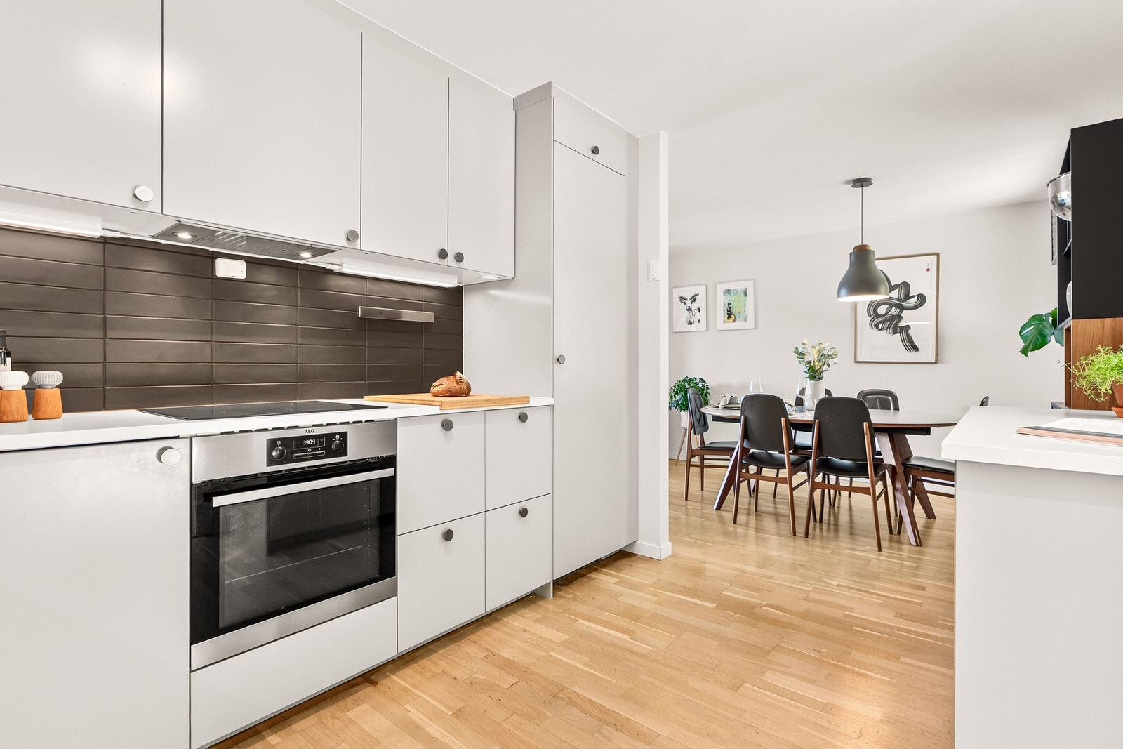 Lyst kjøkken med moderne hvitevarer, åpen løsning mot spisestue og parkettgulv. Galleribilde