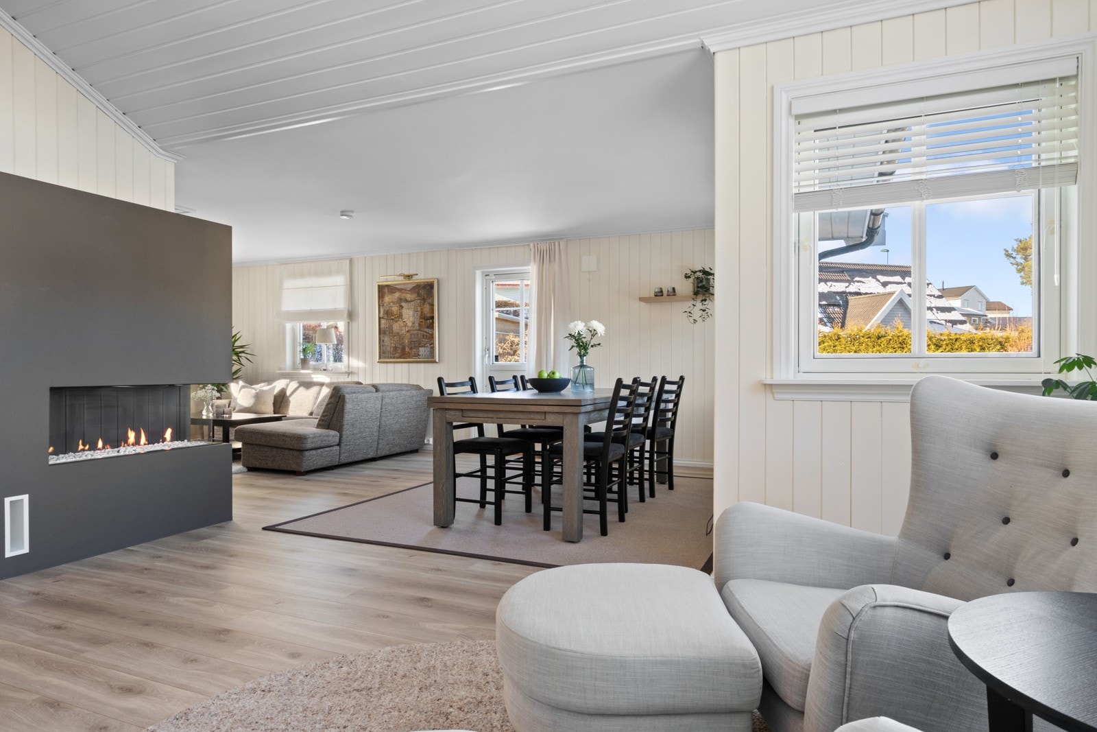 Den vinklede planløsningen gir fine, definerte soner for møblering, og sentralt i rommet er det en moderne gasspeis fra 2019. Galleribilde