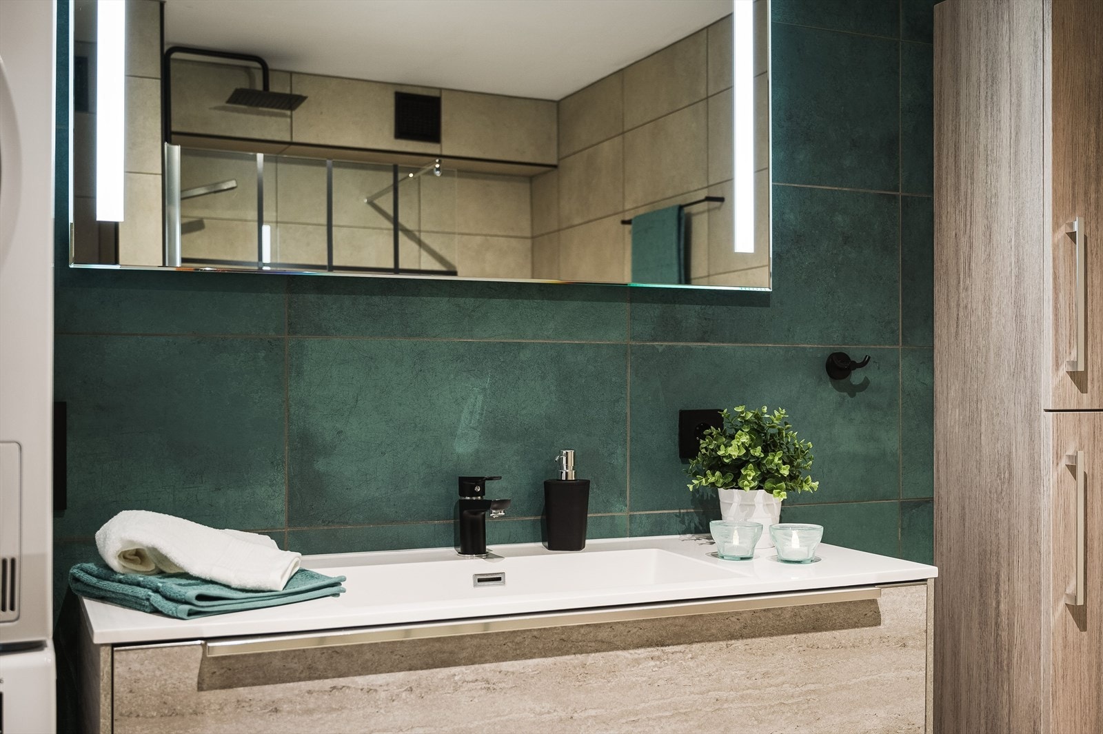 Pen baderomsinnredning med heldekkende servant, speilskap med belysning over, samt ekstra vegghengt høyskap ved siden av. Galleribilde