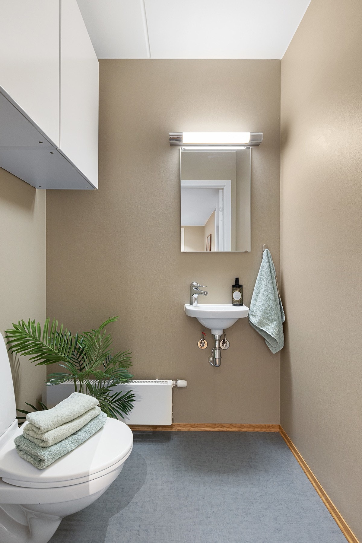 Separat toalettrom pent innredet med vegghengt klosett, servant, radiator og veggskap. Galleribilde