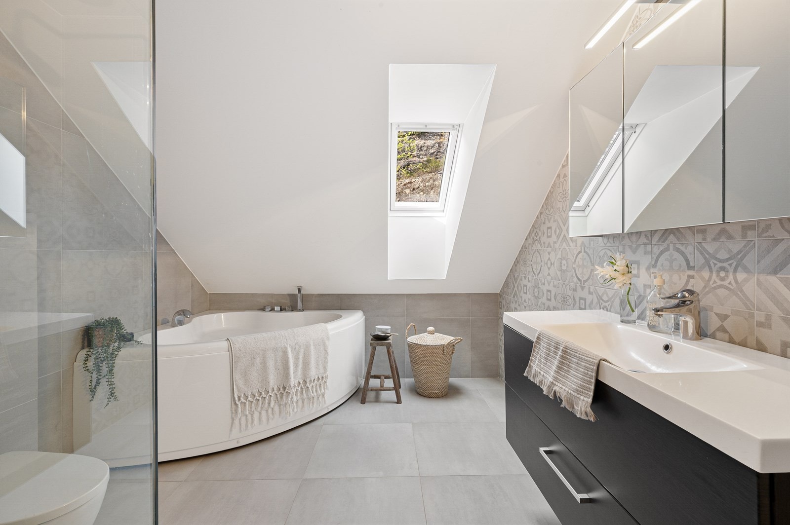 Badet er innredet med badekar, dusjvegger av glass og dusjgarnityr på vegg, vegghengt toalett og innredning med servant. Galleribilde
