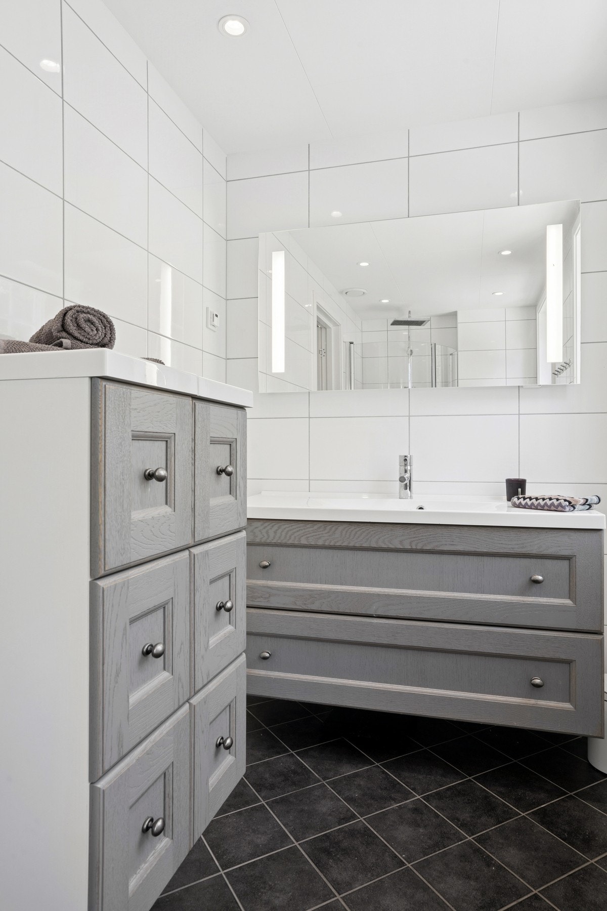 Baderommet er flislagt med moderne innredning med servant, speilskap og belysning, dusj med innfellbare dører og vegghengt toalett. Galleribilde