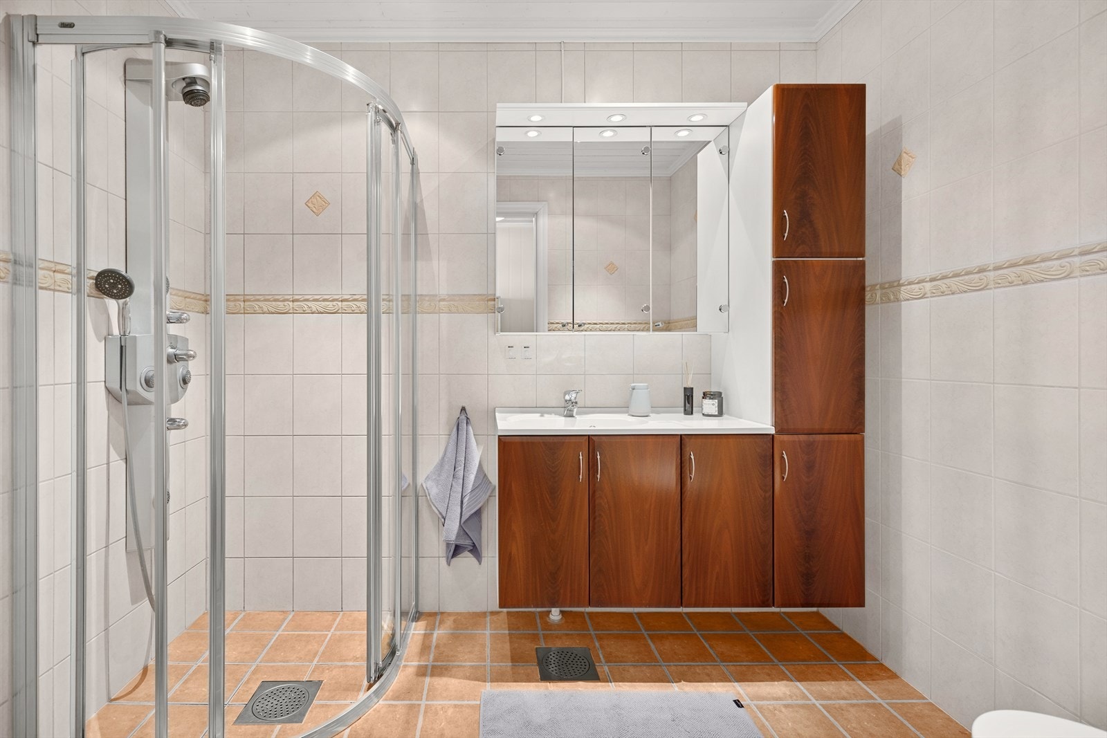 Badet er utstyrt med toalett, dusjhjørne med glassdører, samt innredning med servant og speilskap. Galleribilde