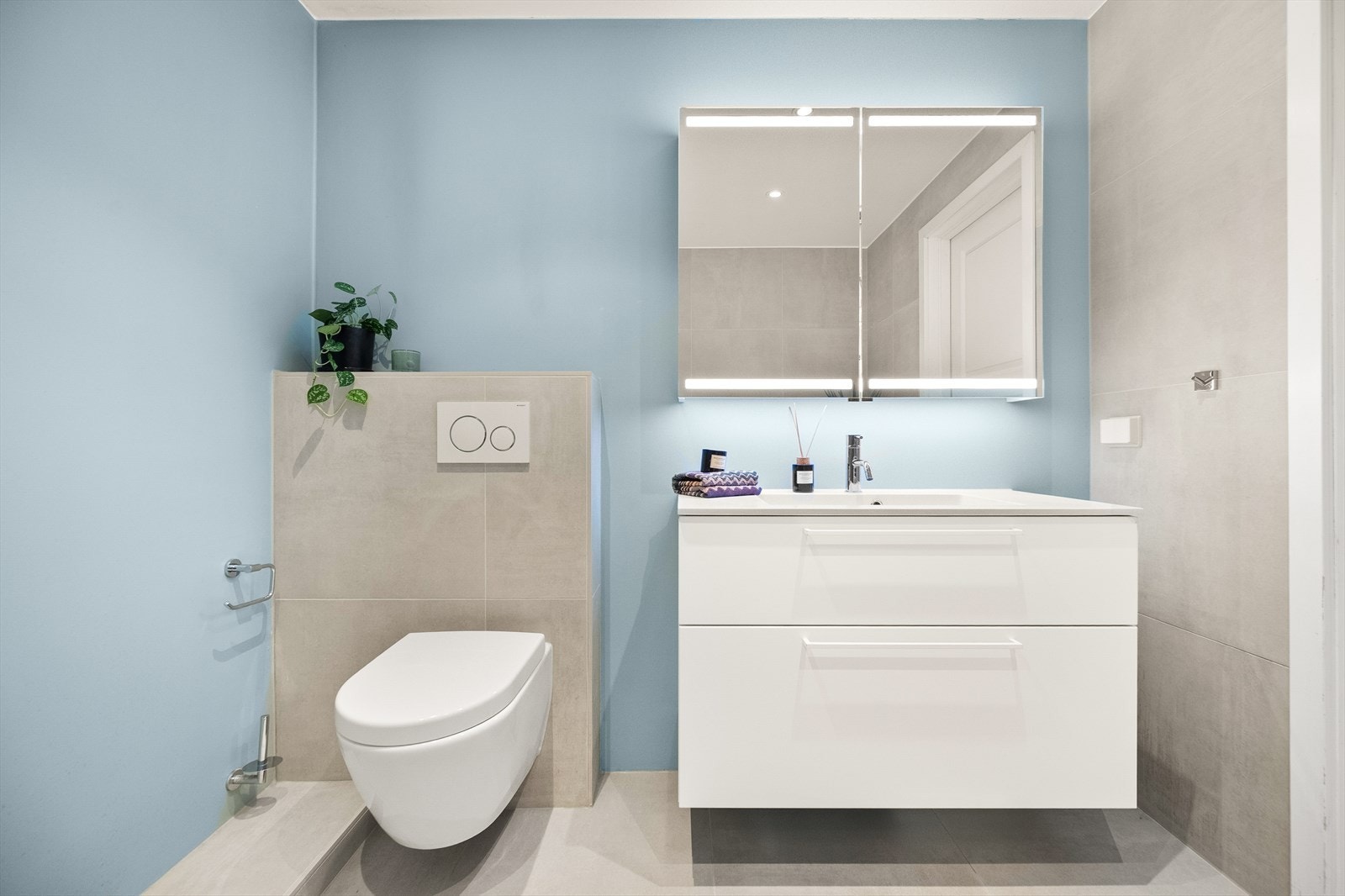 Badet er innredet med vegghengt toalett, dusjhjørne med svingbare glassdører og baderomsinnredning med servant nedfelt i innredning, speilskap m/lys og skuffer. Det er opplegg for vaskemaskin. Galleribilde