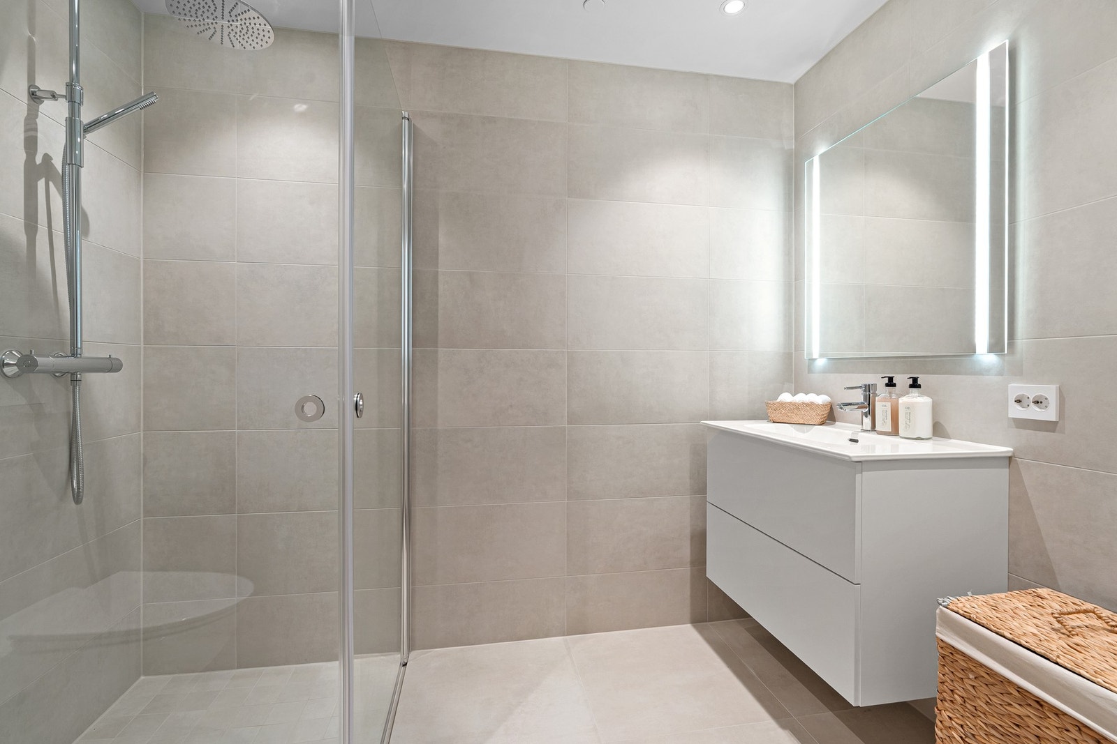 Lekkert fliselagt baderom med servantinnredning, speil m/lys, dusjhjørne, vegghengt wc og opplegg til vaskemaskin. Galleribilde