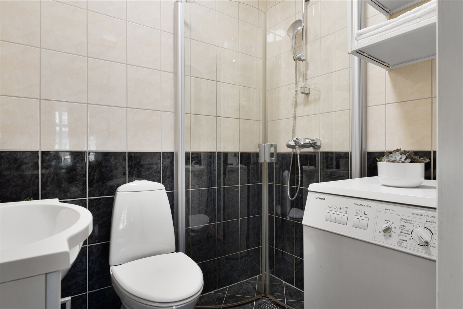 Badet er innredet med dusjdører, servant, toalett, møbler og opplegg for vaskemaskin. Galleribilde