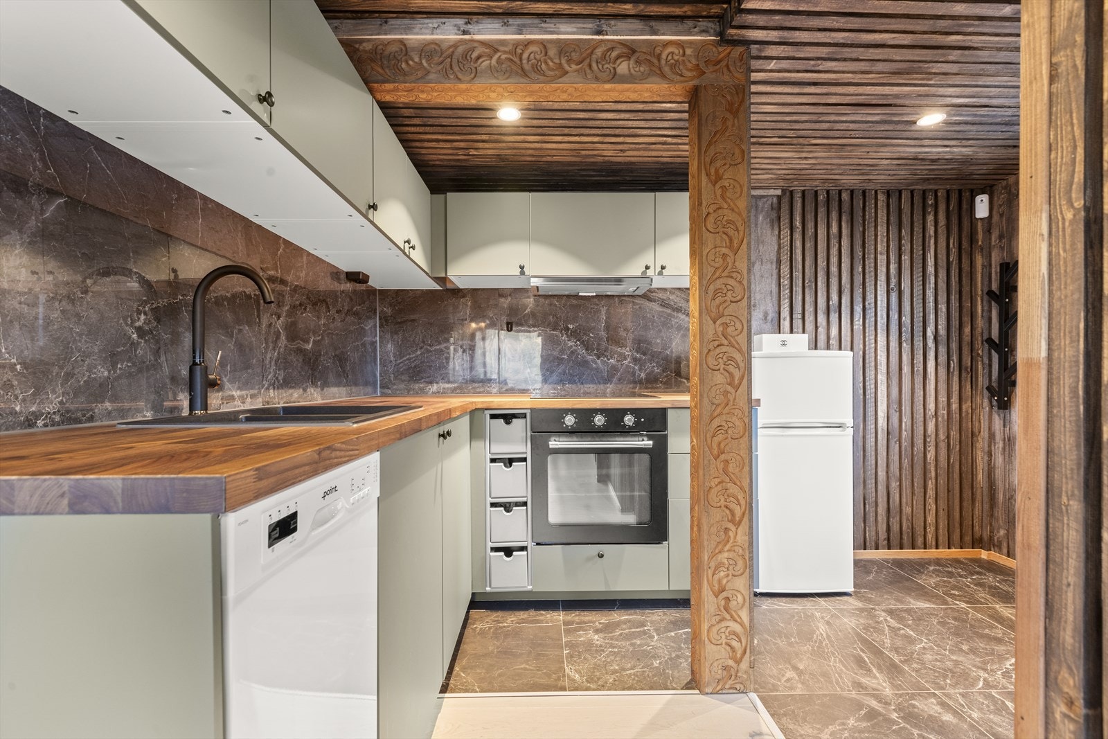 Integrerte hvitevarer som komfyr og platetopp med ventilator over samt oppvaskmaskin plassert i nisje og frittstående kjøleskap. Galleribilde