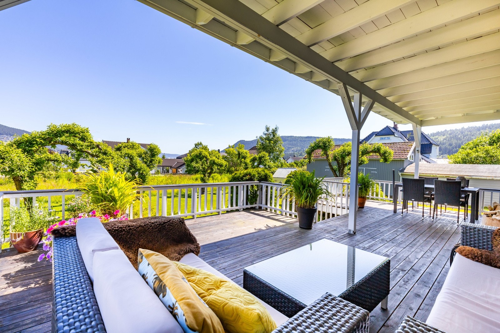 Stor, delvis overbygd terrasse med utsikt over grønne omgivelser og åser i bakgrunnen. God plass til både sittegruppe og spisebord. Galleribilde