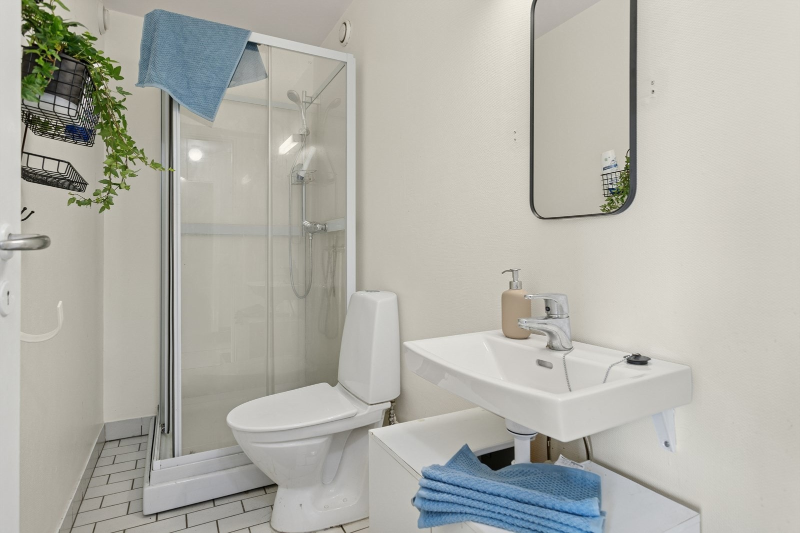 Bad med flislagt gulv, dusjkabinett, toalett og servant med skapplass. Badet varmes opp ved hjelp av varmeovn. Galleribilde