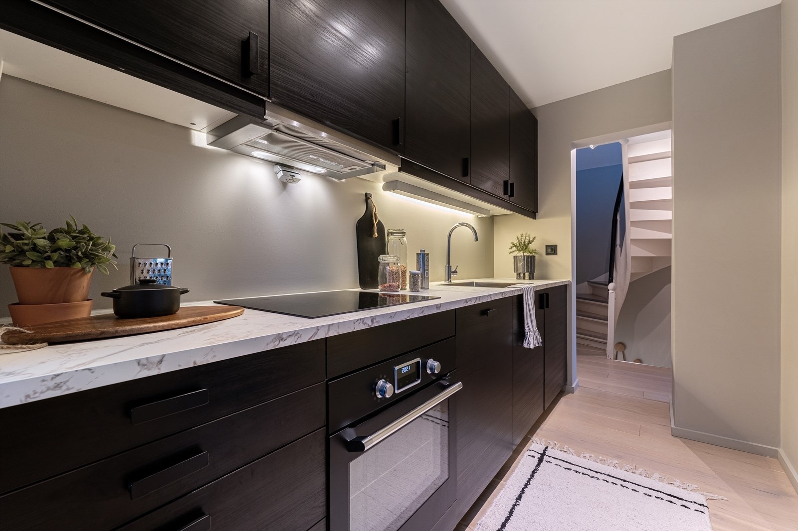 Kjøkkenet er innredet med mørke glatte fronter og laminert benkeplate med nedfelt stålvask og platetopp Galleribilde