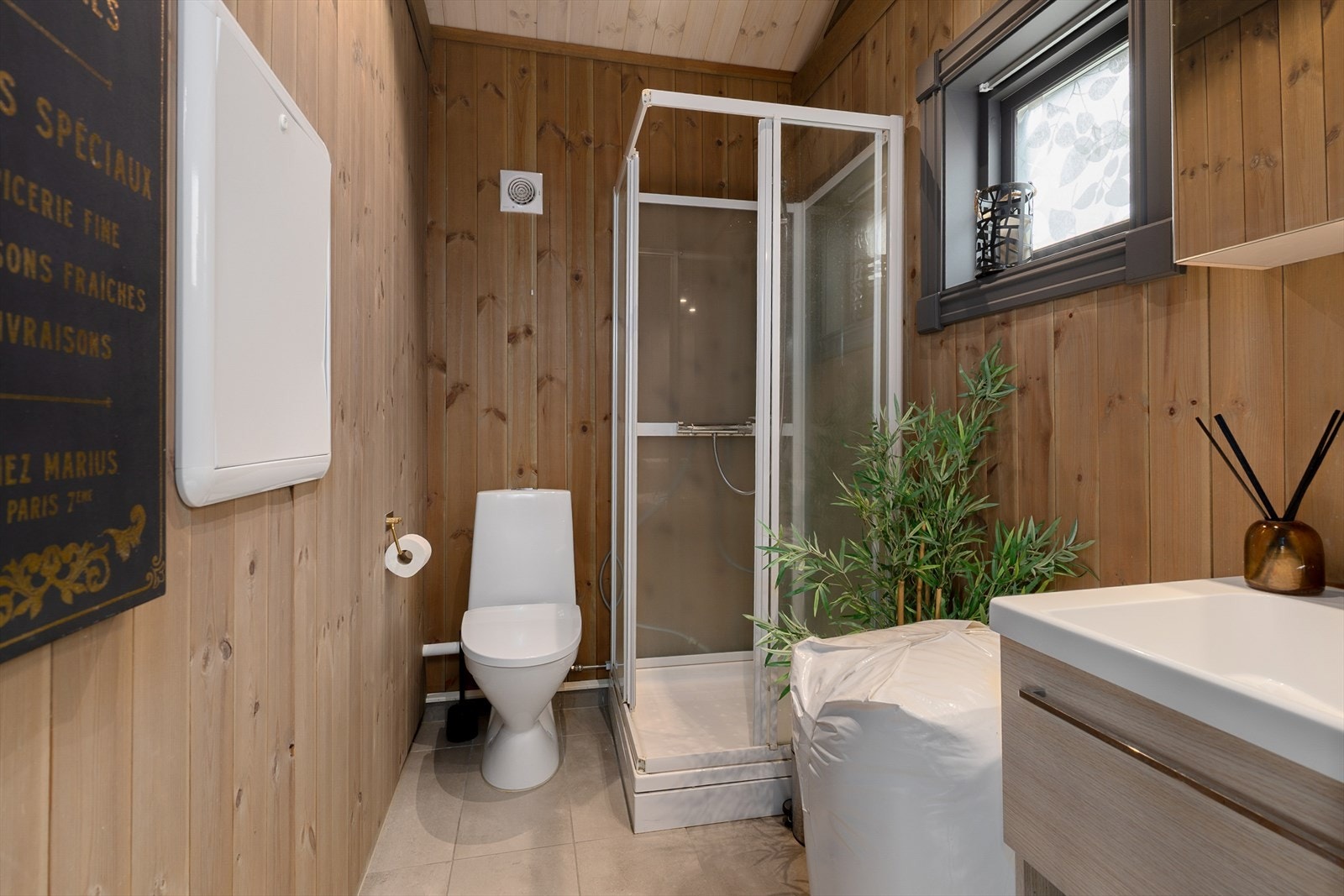 Flislagt baderom med elektriske varmekabler i gulv, panel på vegger og himling. Badet er utstyrt med servant med underskap, dusjkabinett og gulvmontert wc. Det er elektrisk styrt vifte. Galleribilde