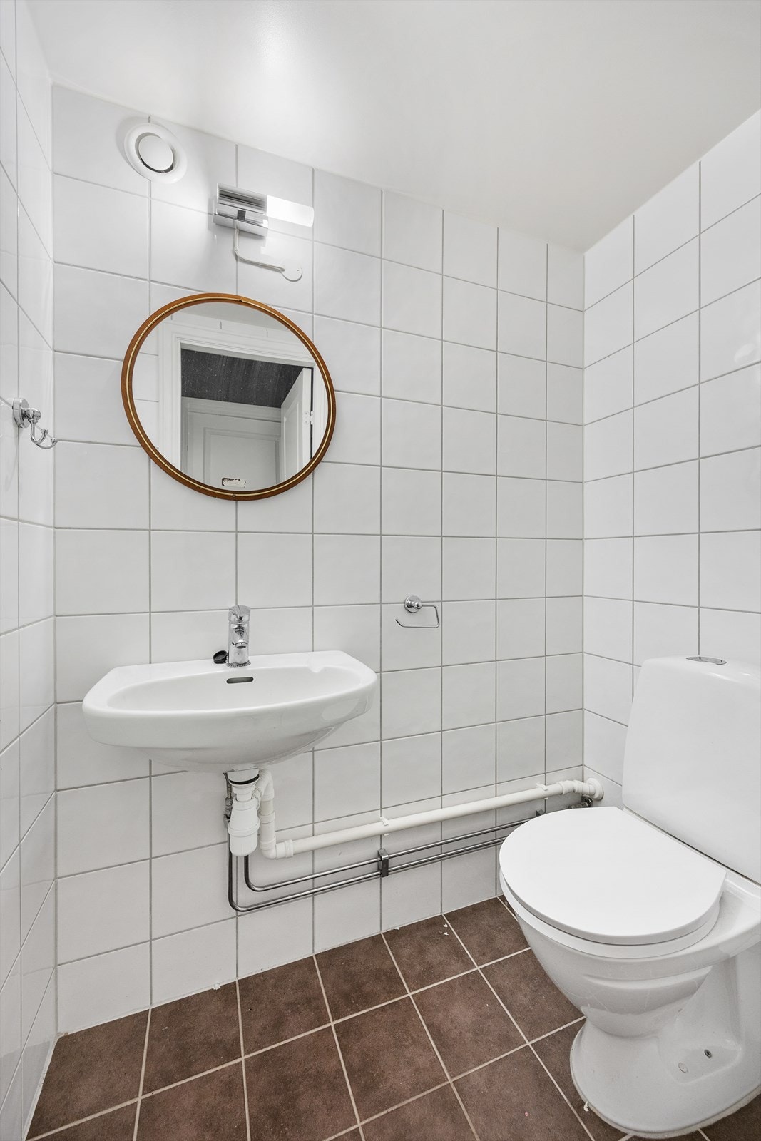 Separat wc-rom med flislagte overflater, utstyrt med gulvstående wc og enkel servant Galleribilde