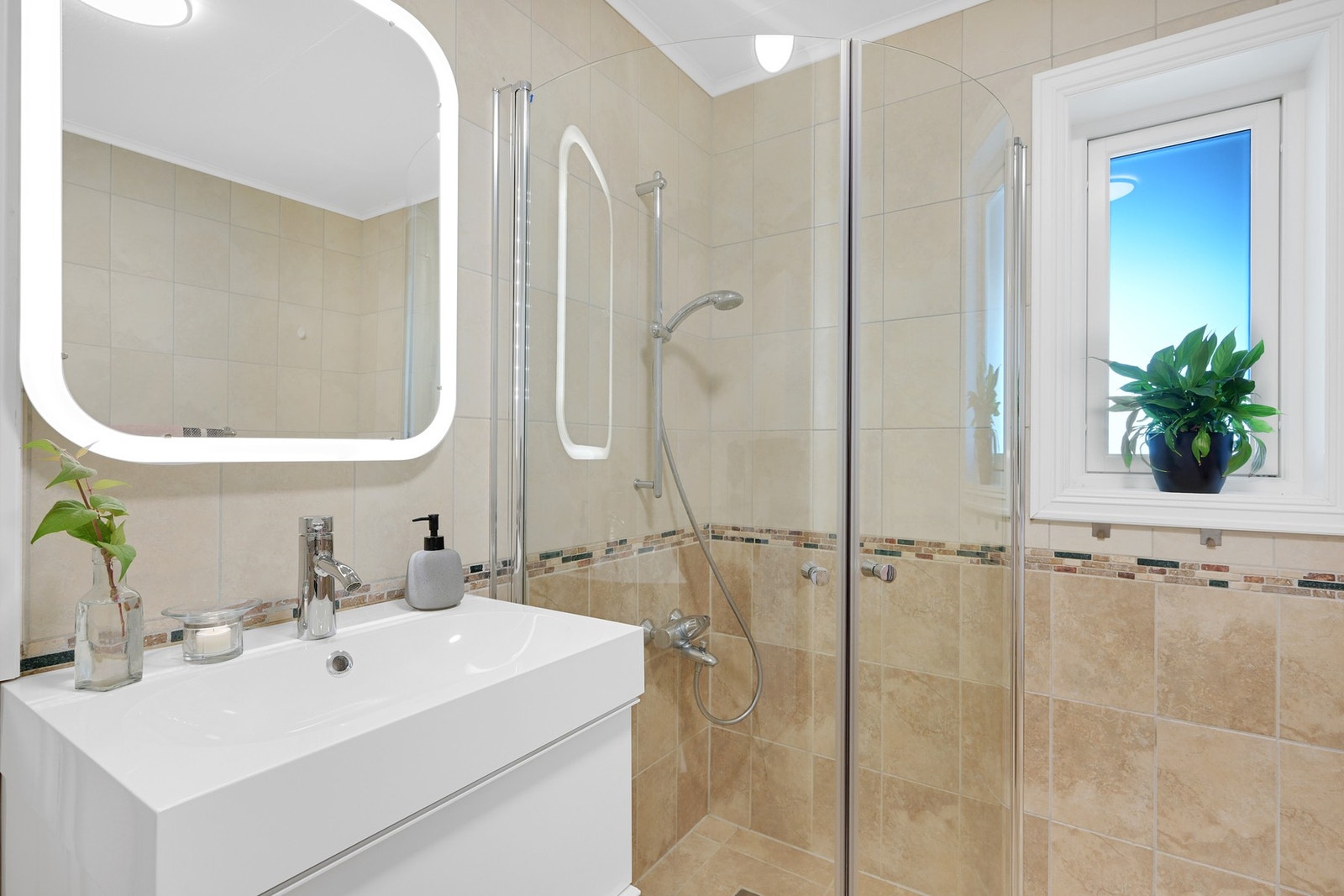 Badet inneholder servant med baderomsinnredning, dusjhjørne med buede dører og opplegg for vaskemaskin. Galleribilde